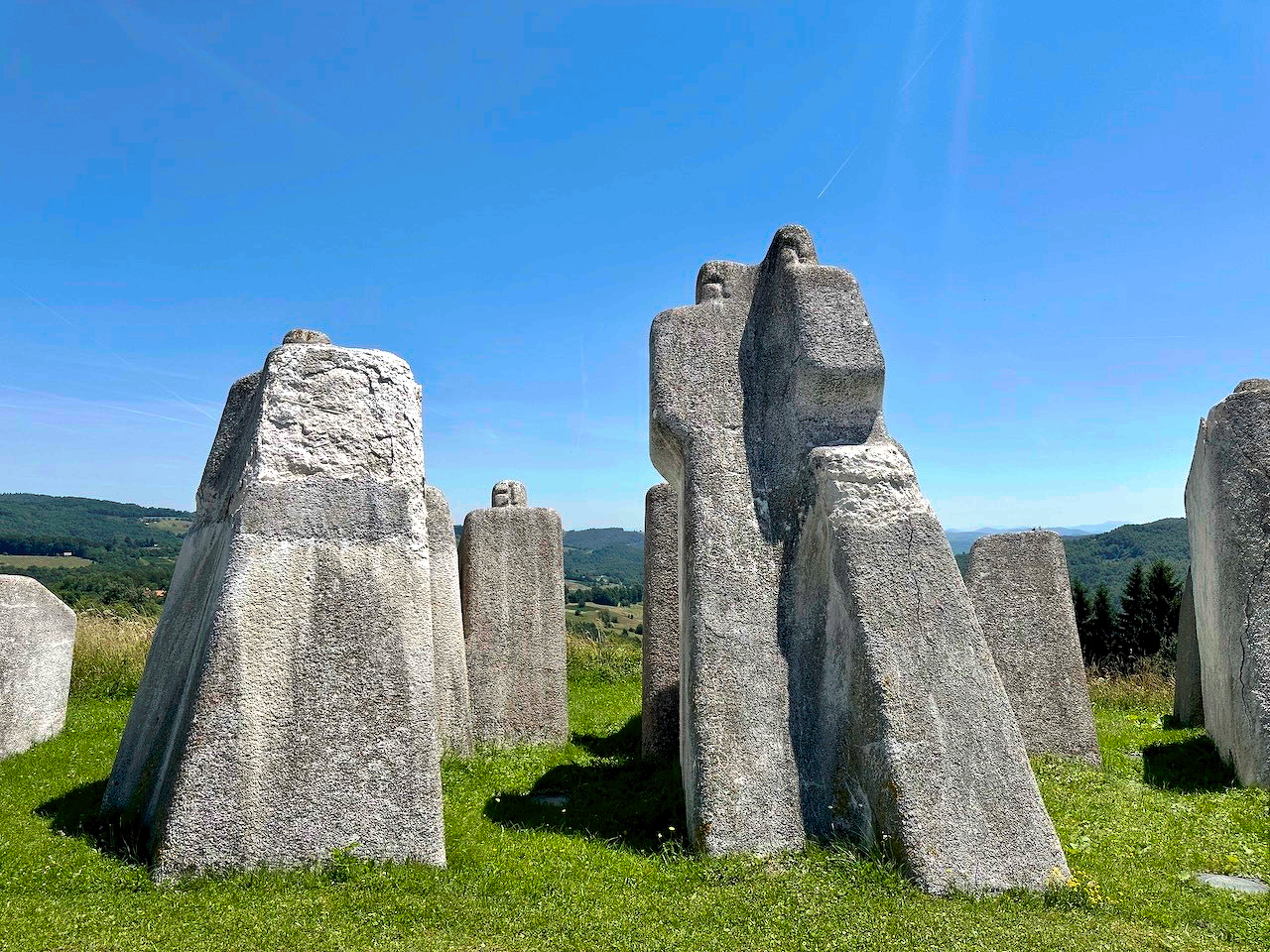 Large, abstract stone sculptures stand on a grassy field under a clear blue sky.