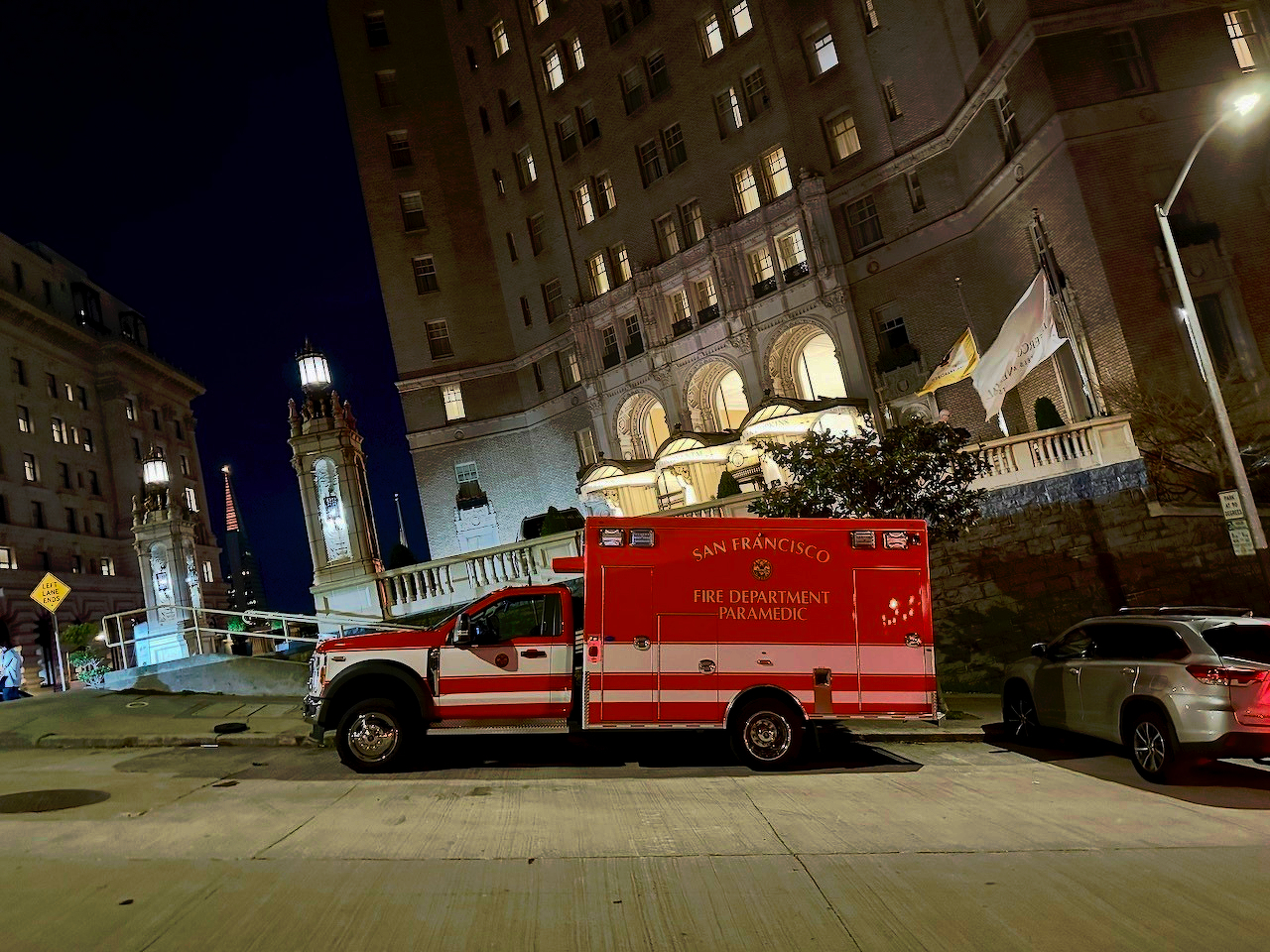 A San Francisco Fire Department paramedic vehicle is parked on a street at night in front of a historic building.