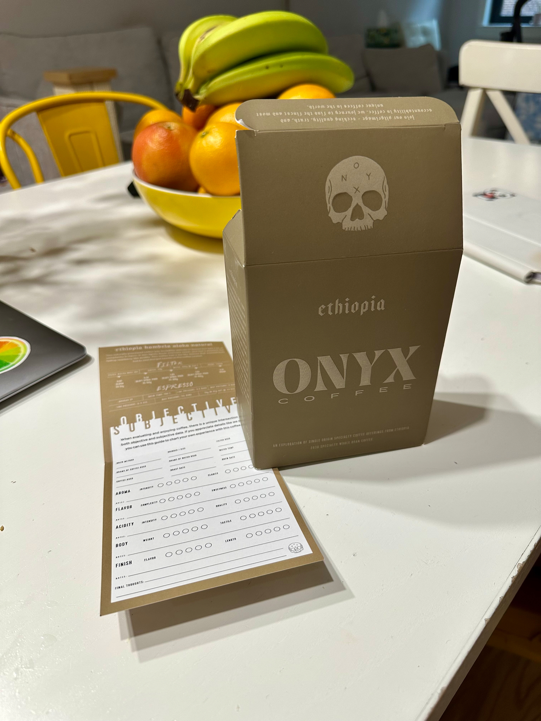 A box of Onyx Coffee with a tasting guide is displayed on a table next to a bowl of fruit.
