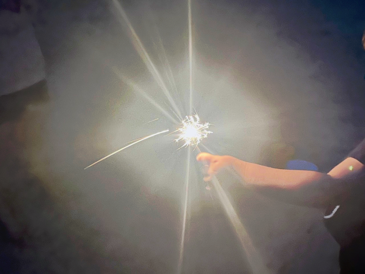 A hand is holding a lit sparkler, creating a bright, radiant effect against a dark background.