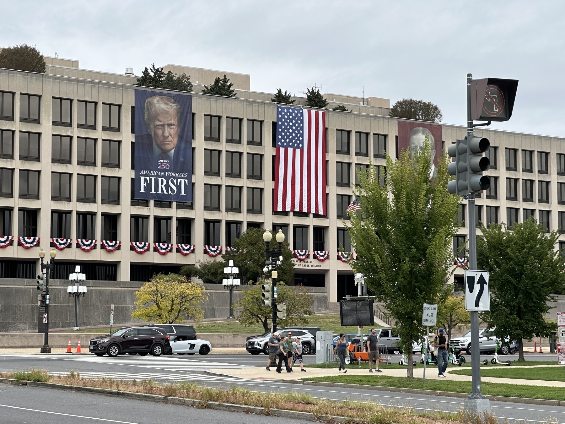 US Department of Labor building in Washington DC adorned with a US flag next to a 3-story high banner with Donald Trump’s severe-looking unsmiling face and the words “American workers FIRST” below.