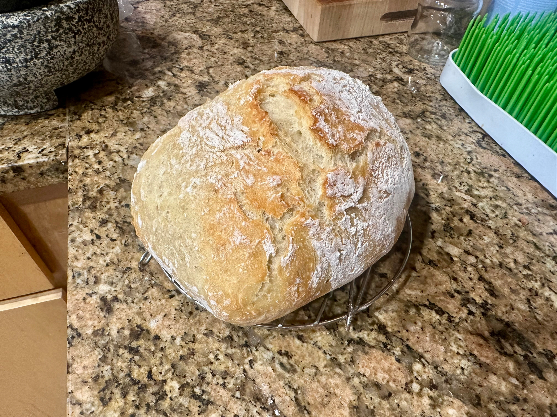A freshly baked loaf of bread rests on a wire rack on a kitchen counter.
