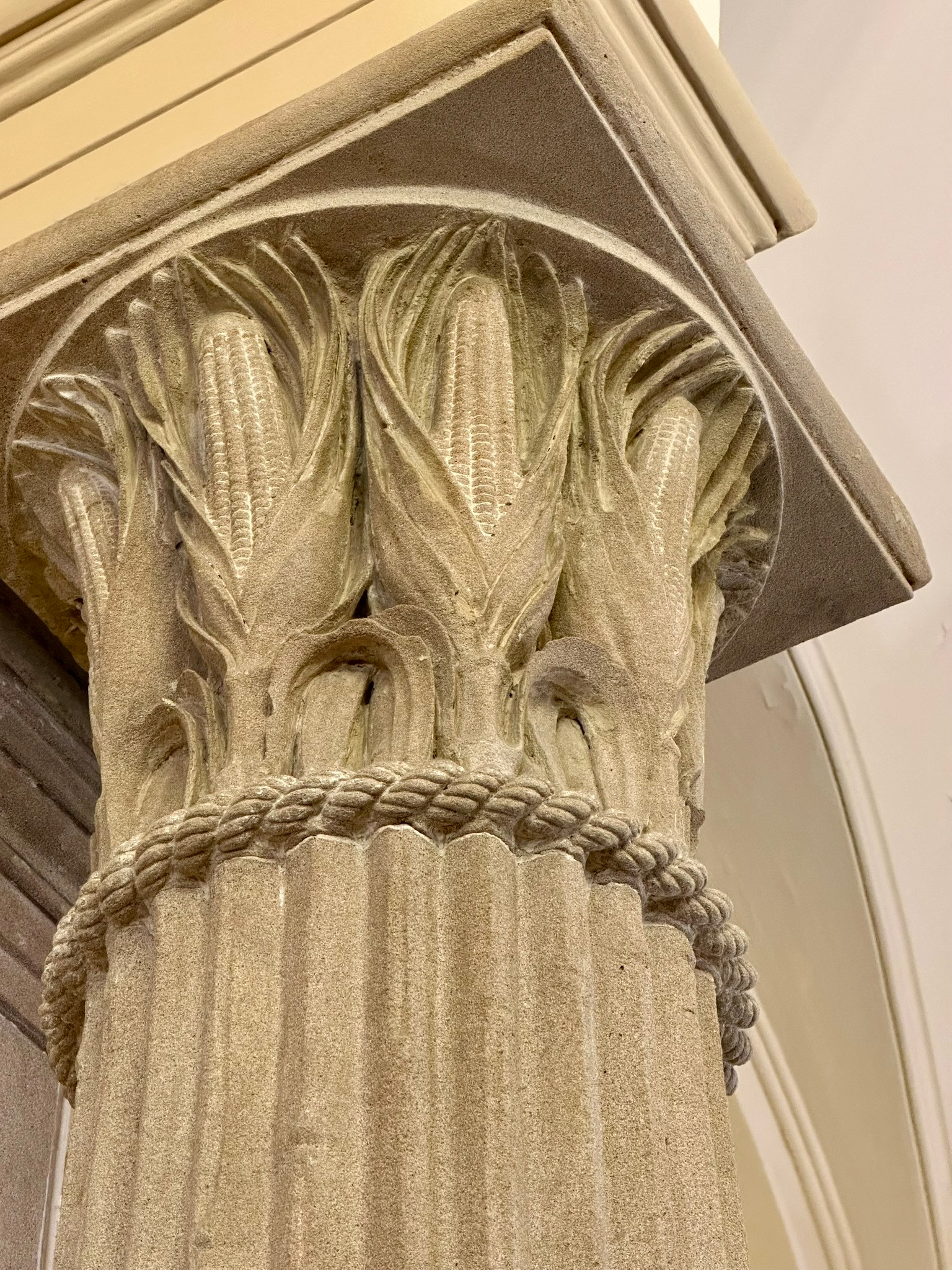 Close up shot of the top of a Corinthian column with ears of corn instead of the usual ornaments.