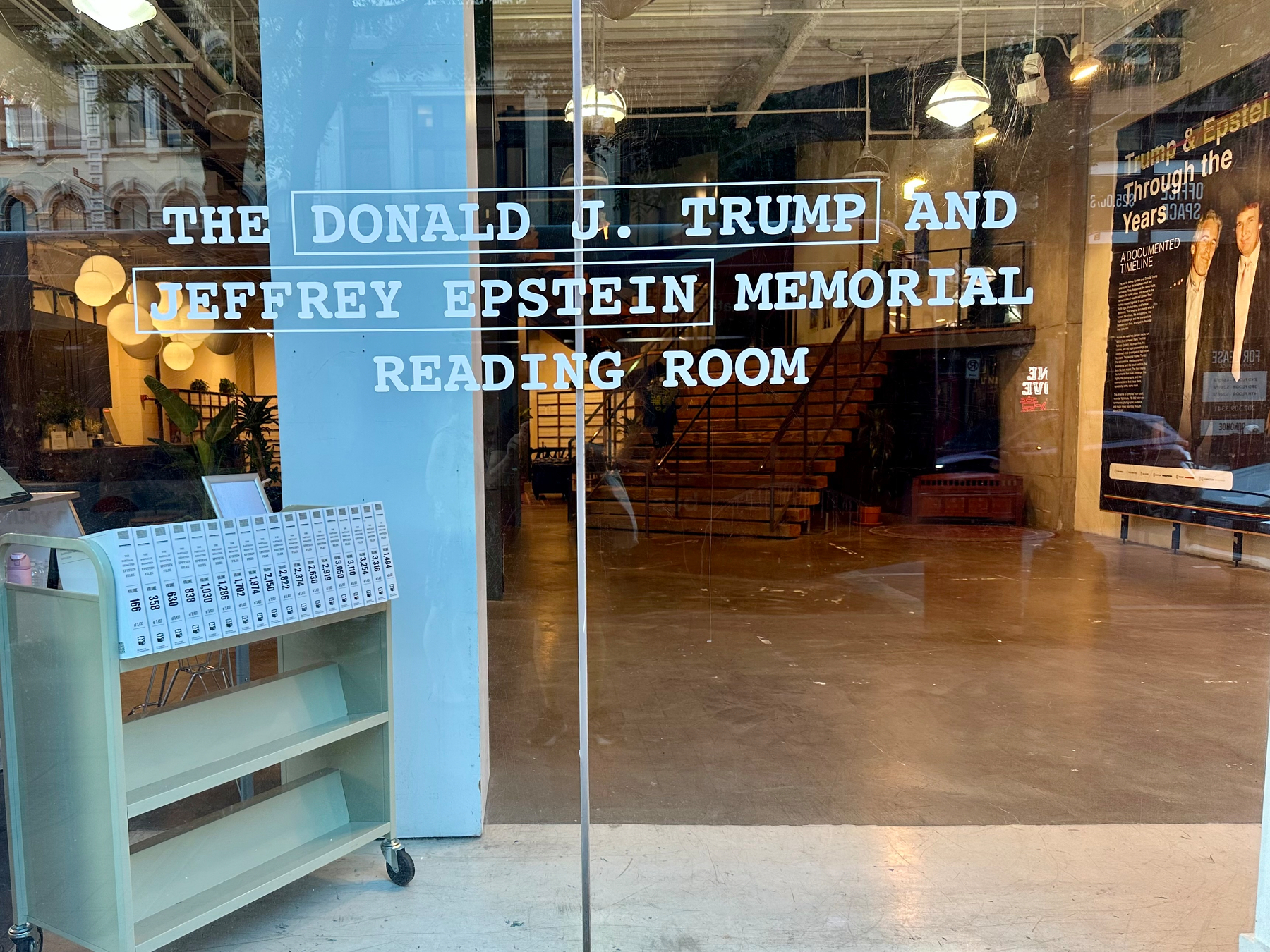 A reading room with a sign “The Donald J. Trump and Jeffrey Epstein Memorial Reading Room” is visible through a glass door.