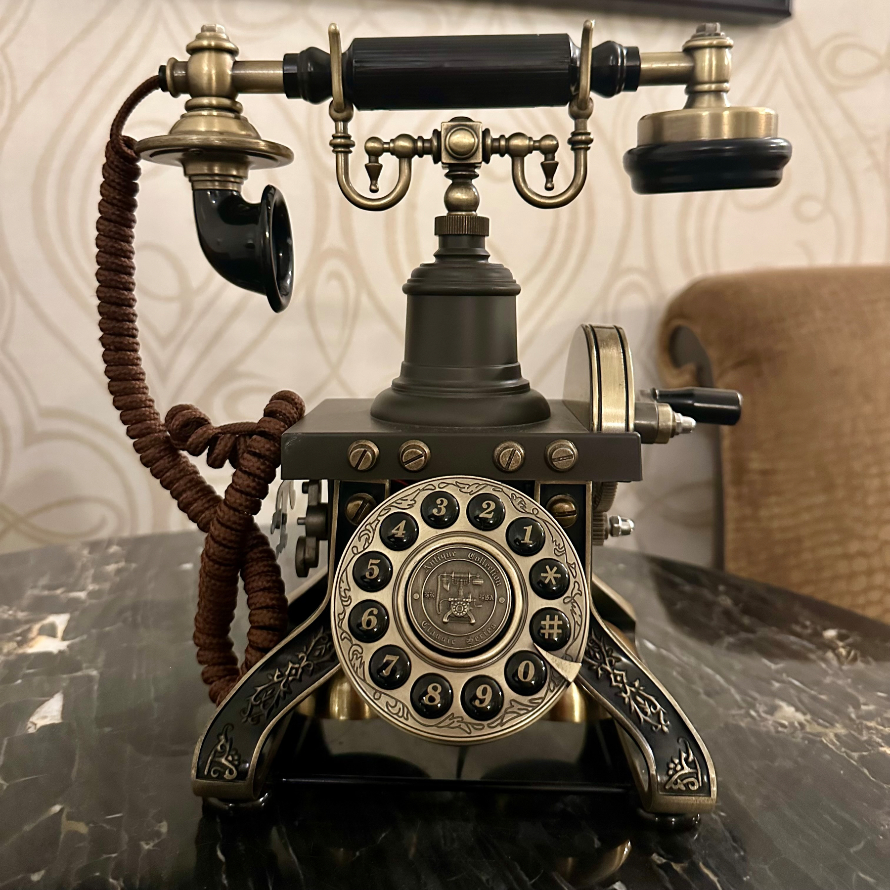 An ornate, seemingly vintage rotary telephone is placed on a marble surface.