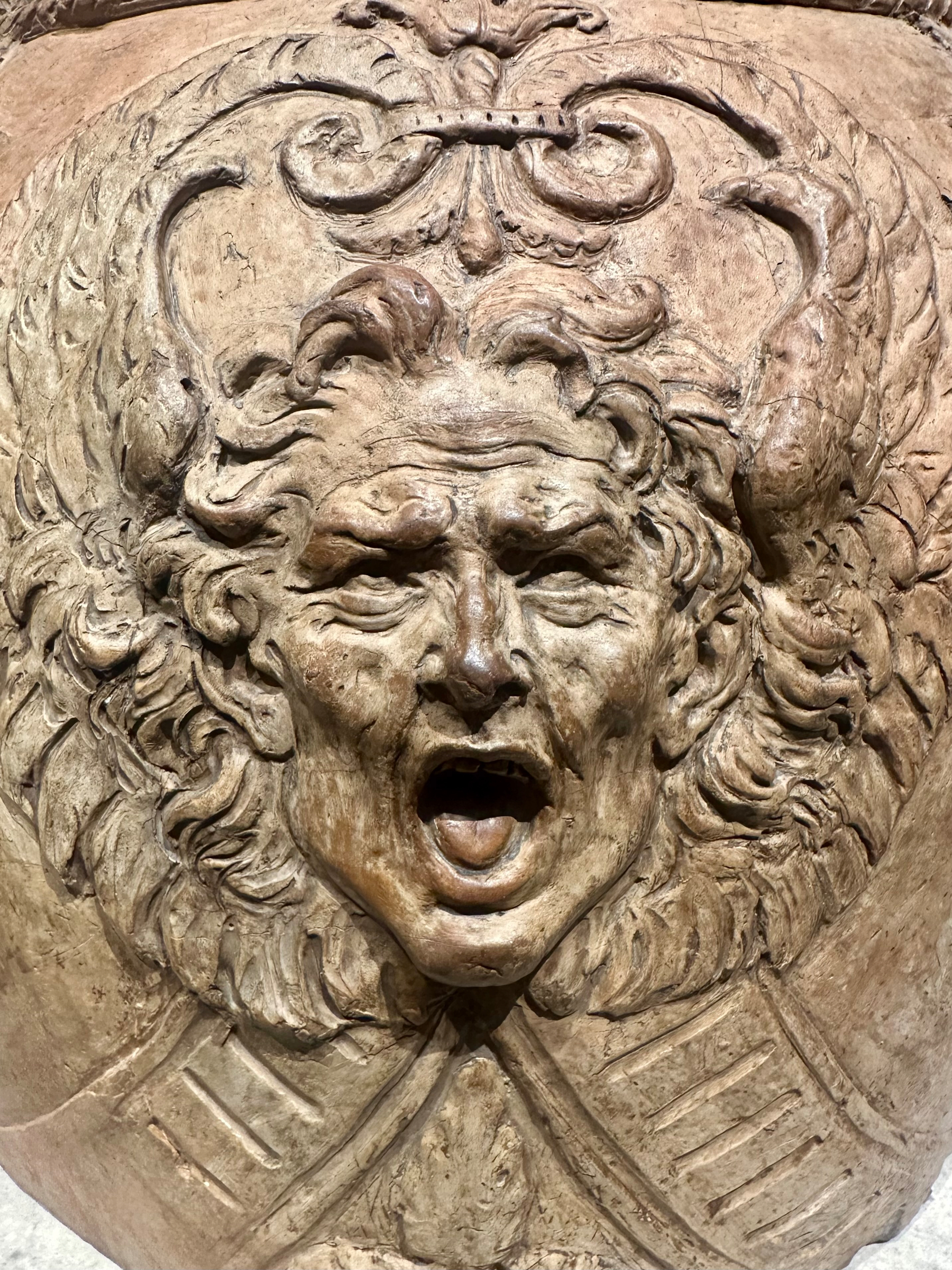 A detailed stone carving depicts a mythical or dramatic face with an open mouth, surrounded by ornate leaf designs.
