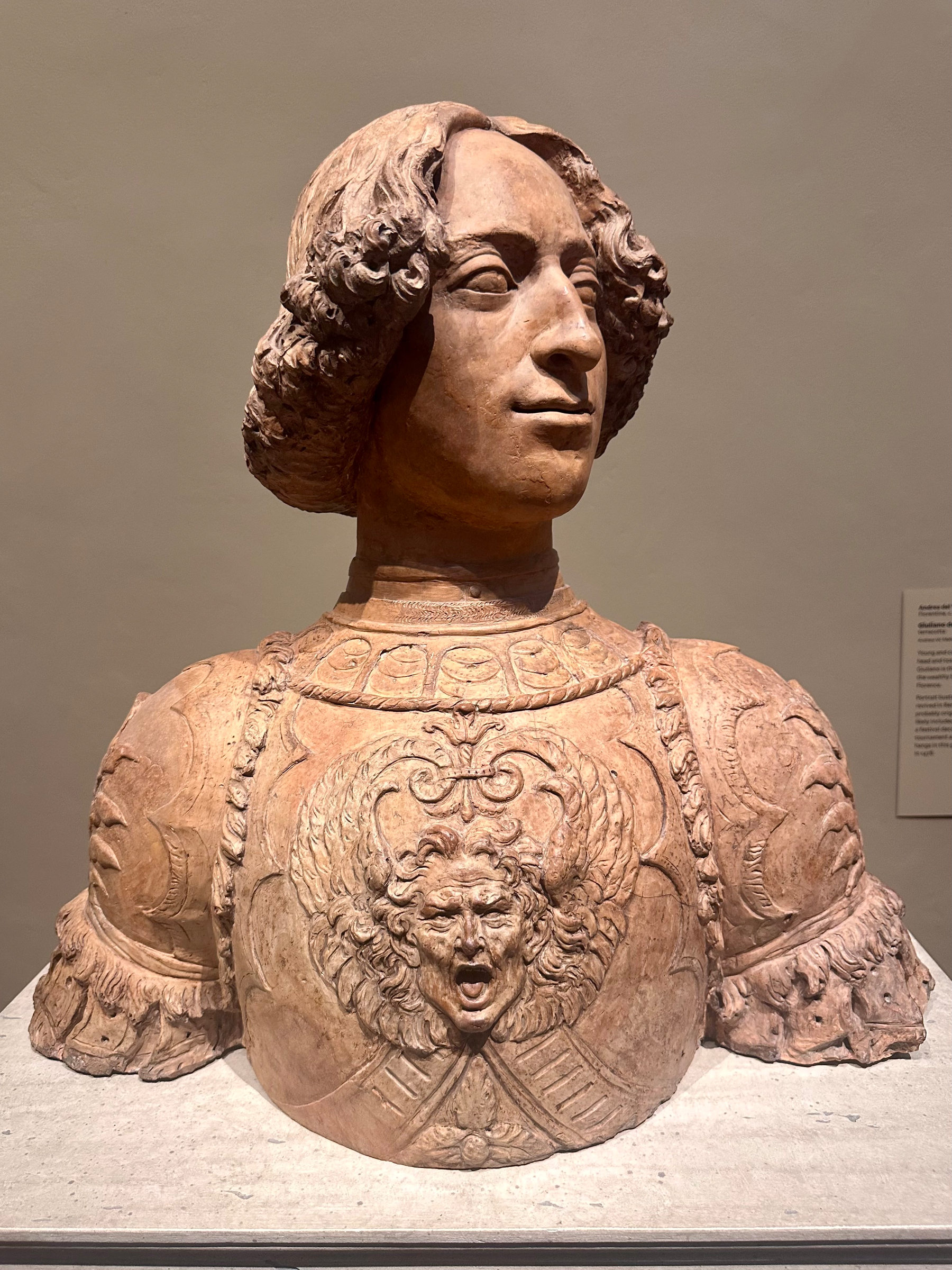 A terracotta bust depicts a person in ornate armor with a detailed, expressive face at the center.