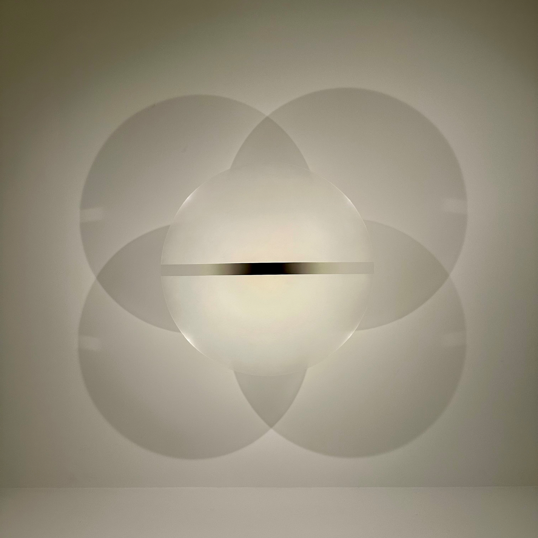 A geometric light fixture on a wall creates overlapping circular shadows in a pattern.
