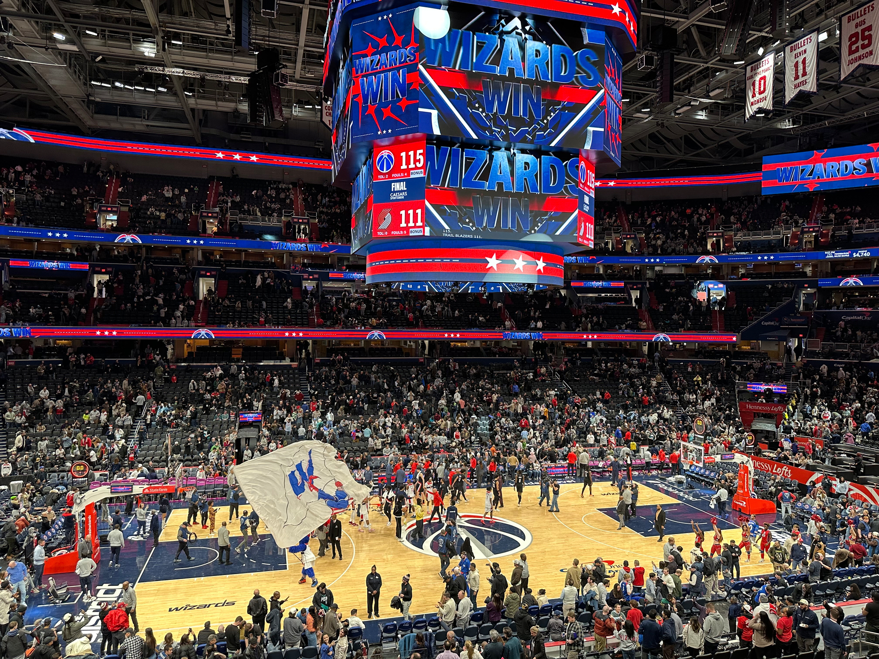 A basketball game has just ended with the Washington Wizards winning, as shown by the scoreboard and ceiling display above the court.