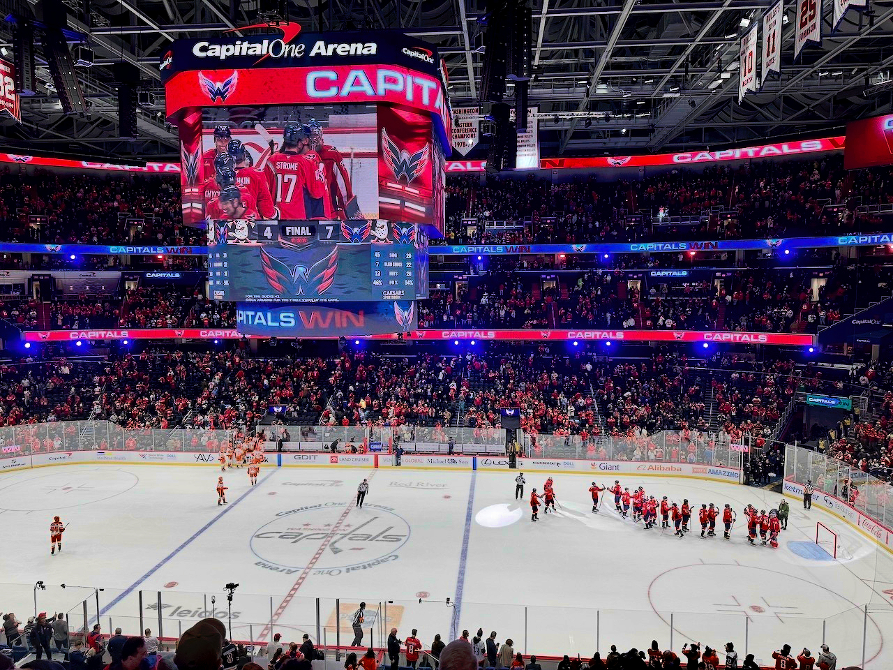 A professional hockey game has just ended at Capital One Arena, with players gathering on the ice and fans leaving the stands.