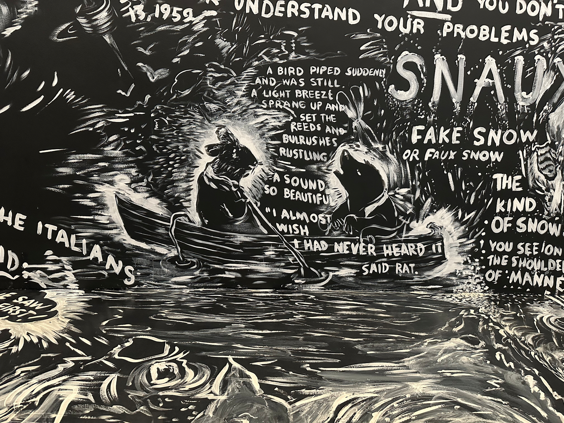 A chalk drawing on a black wall and floor depicts a scene with two animals in a boat accompanied by text.