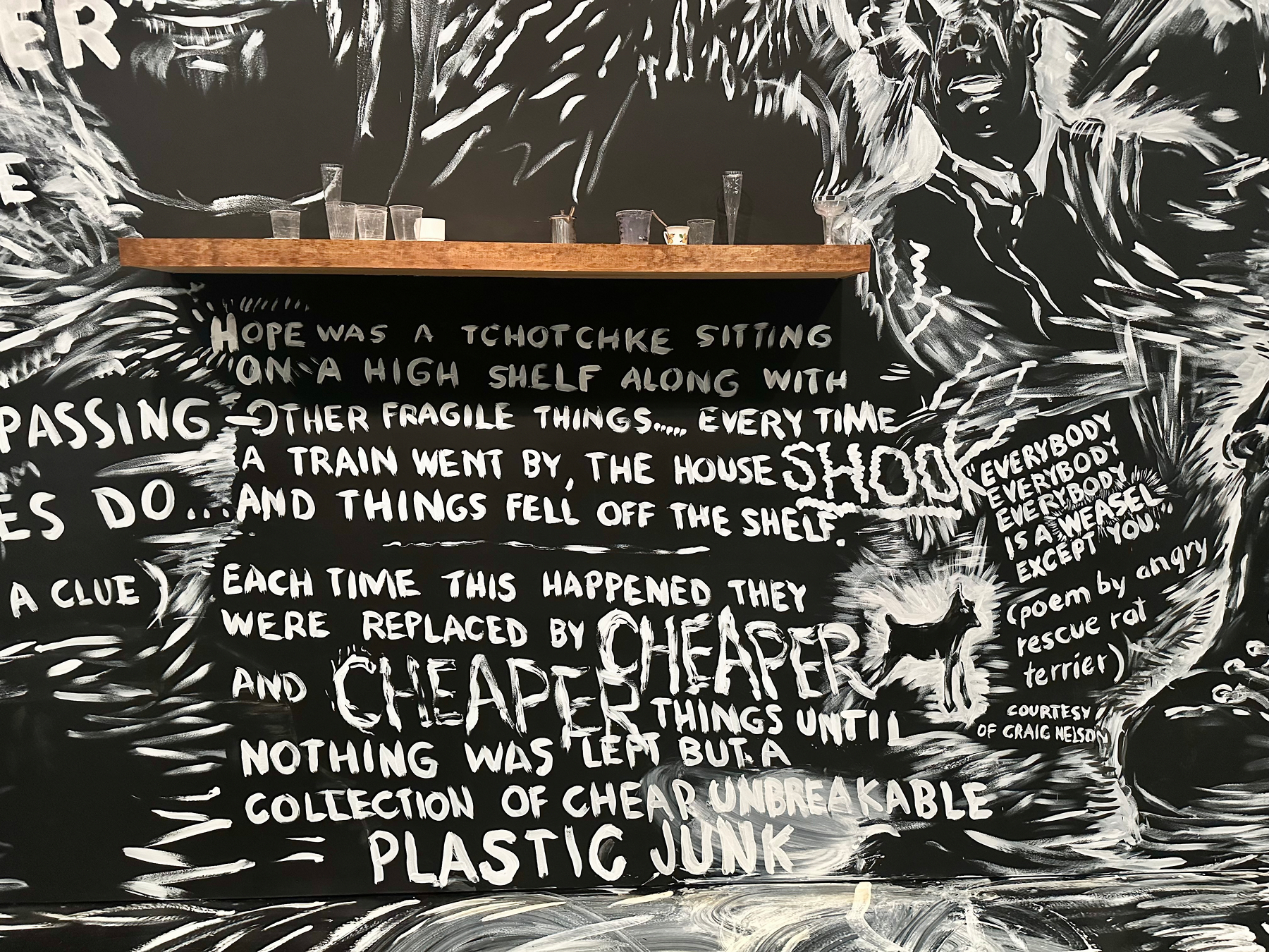 A mural featuring a shelf with small items and a text-heavy, artistic background incorporating a poem and various phrases.