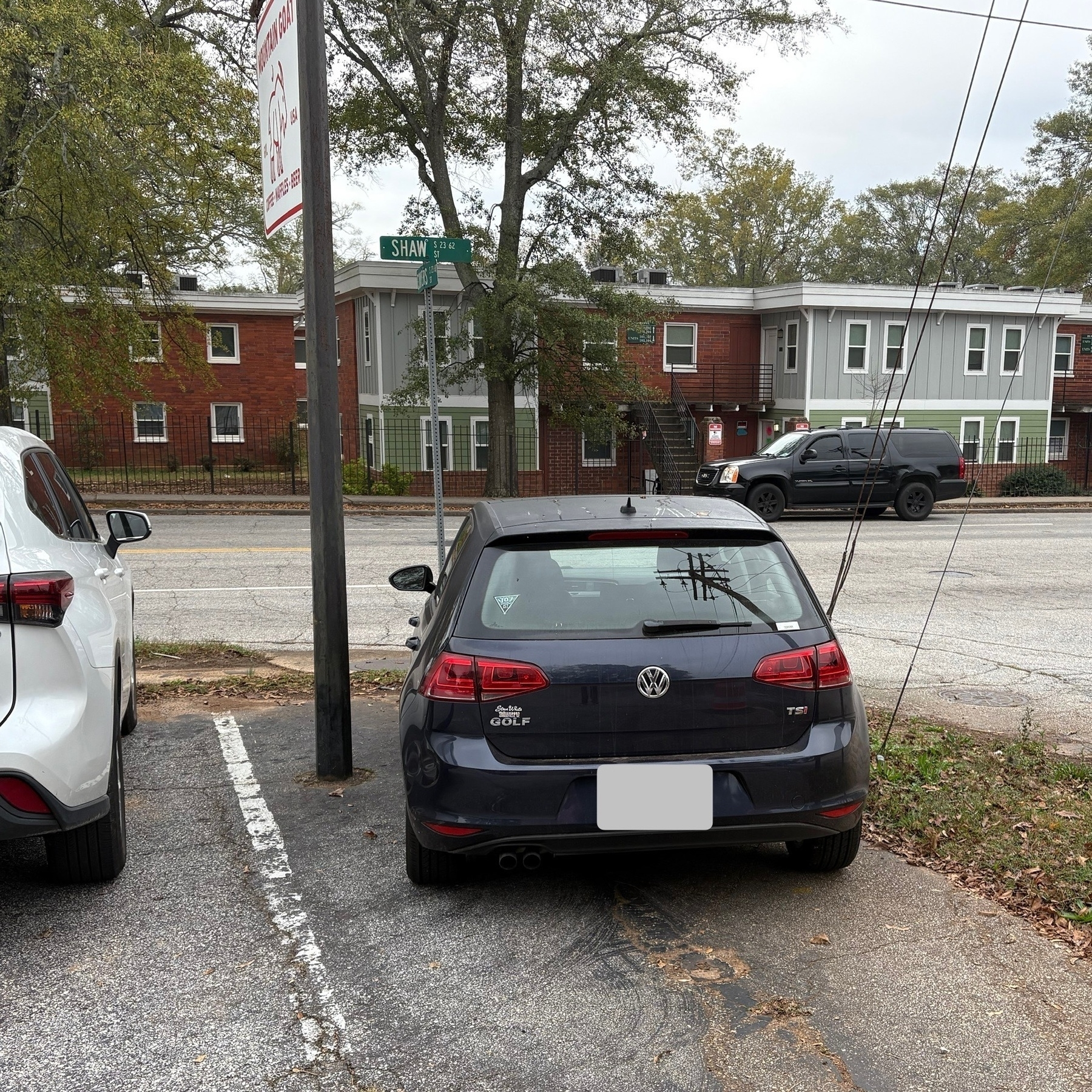 A dark blue Volkswagen Golf parked at an angle inside a parking spot. The spot has the business’ roadside sign inside it, reducing the available space and making the spot non-viable for larger cars. The Golf is tucked nicely between the sign pole on the left and a set of utility pole tethers on the right with just enough space to open the drivers side door.