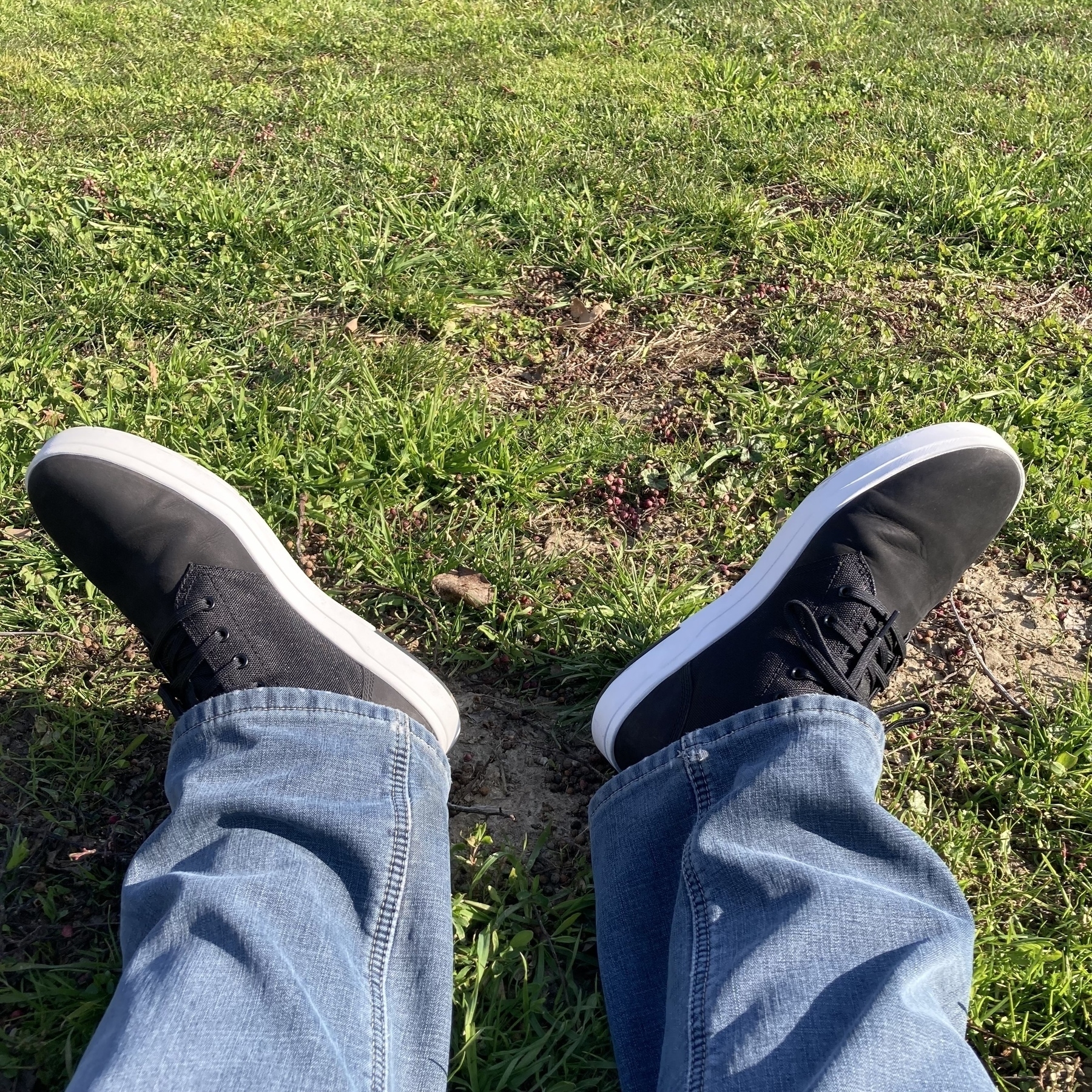 A person is sitting on grass with legs stretched out, wearing blue jeans and black sneakers.