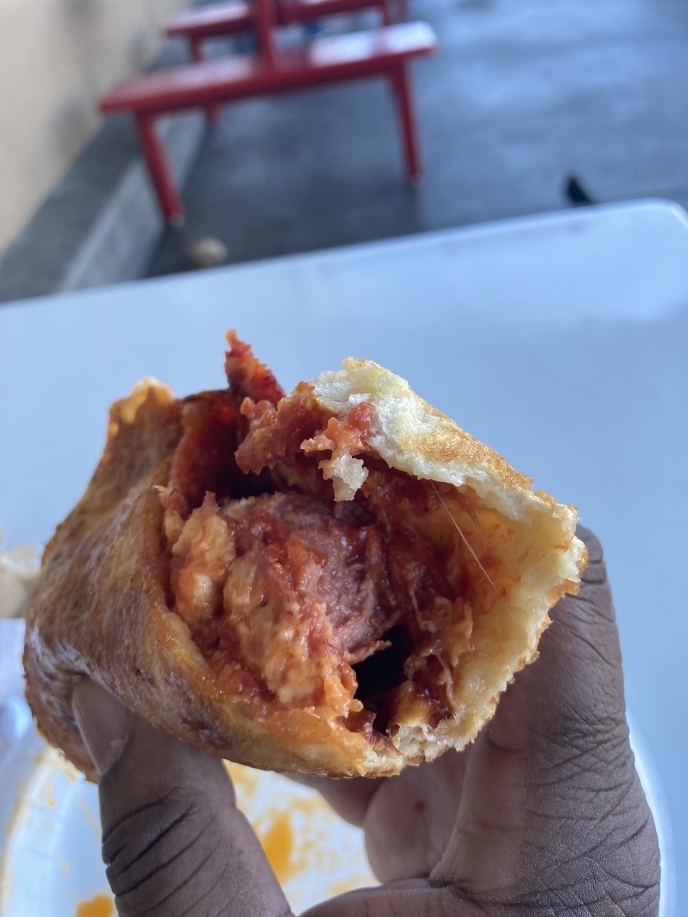 A hand is holding a partially eaten, filling-stuffed pastry over a table, with red seating in the background.