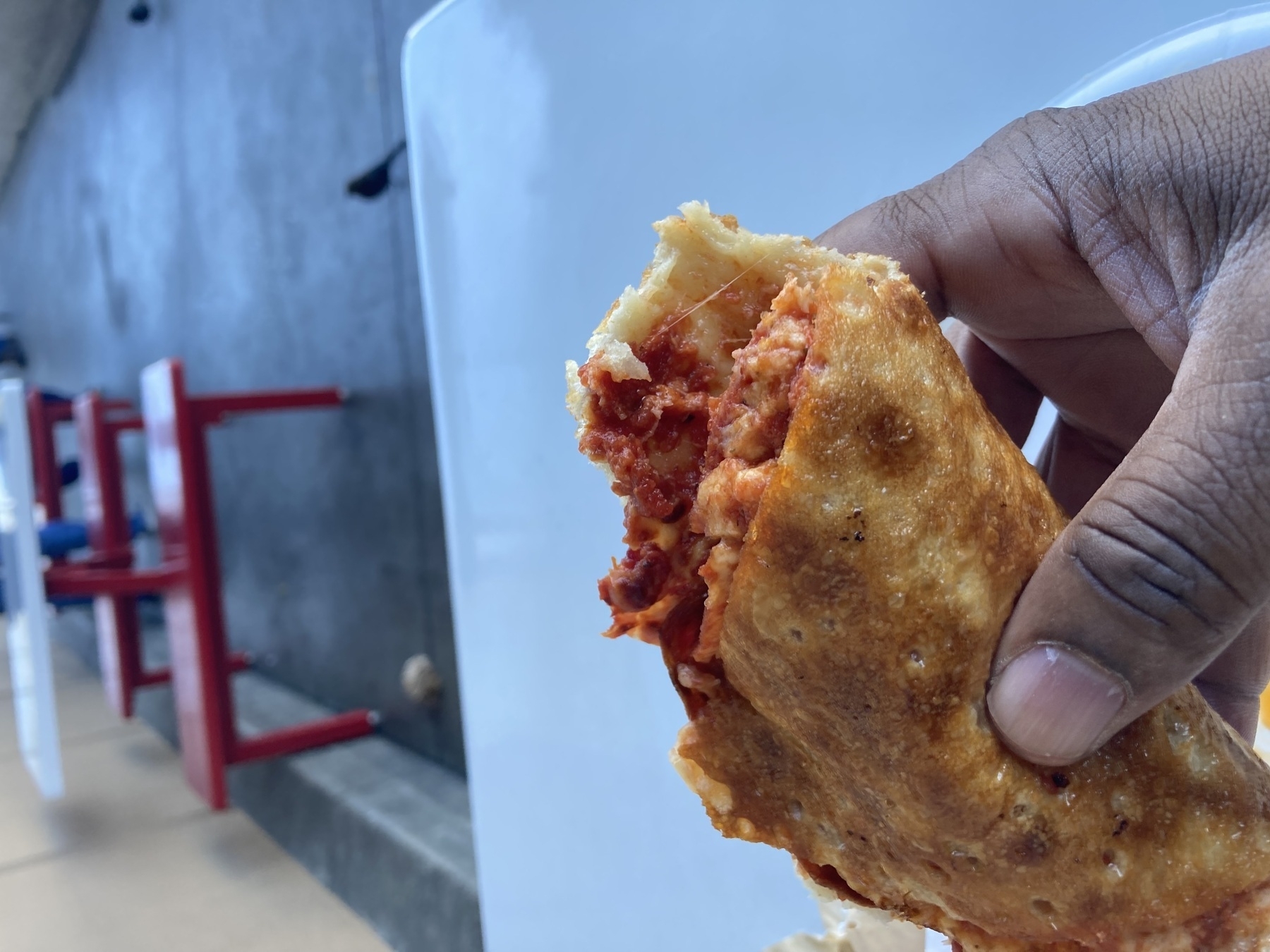 A hand is holding a partially eaten pastry filled with a reddish filling, likely a type of sandwich or empanada.