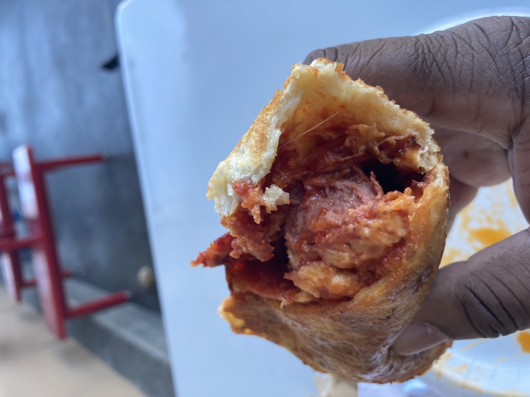 A person is holding a partially eaten pastry filled with a red, meat-like filling.