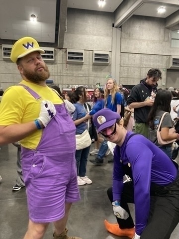 Two people are dressed in costumes resembling characters from a popular video game series, posing playfully in a busy indoor event.
