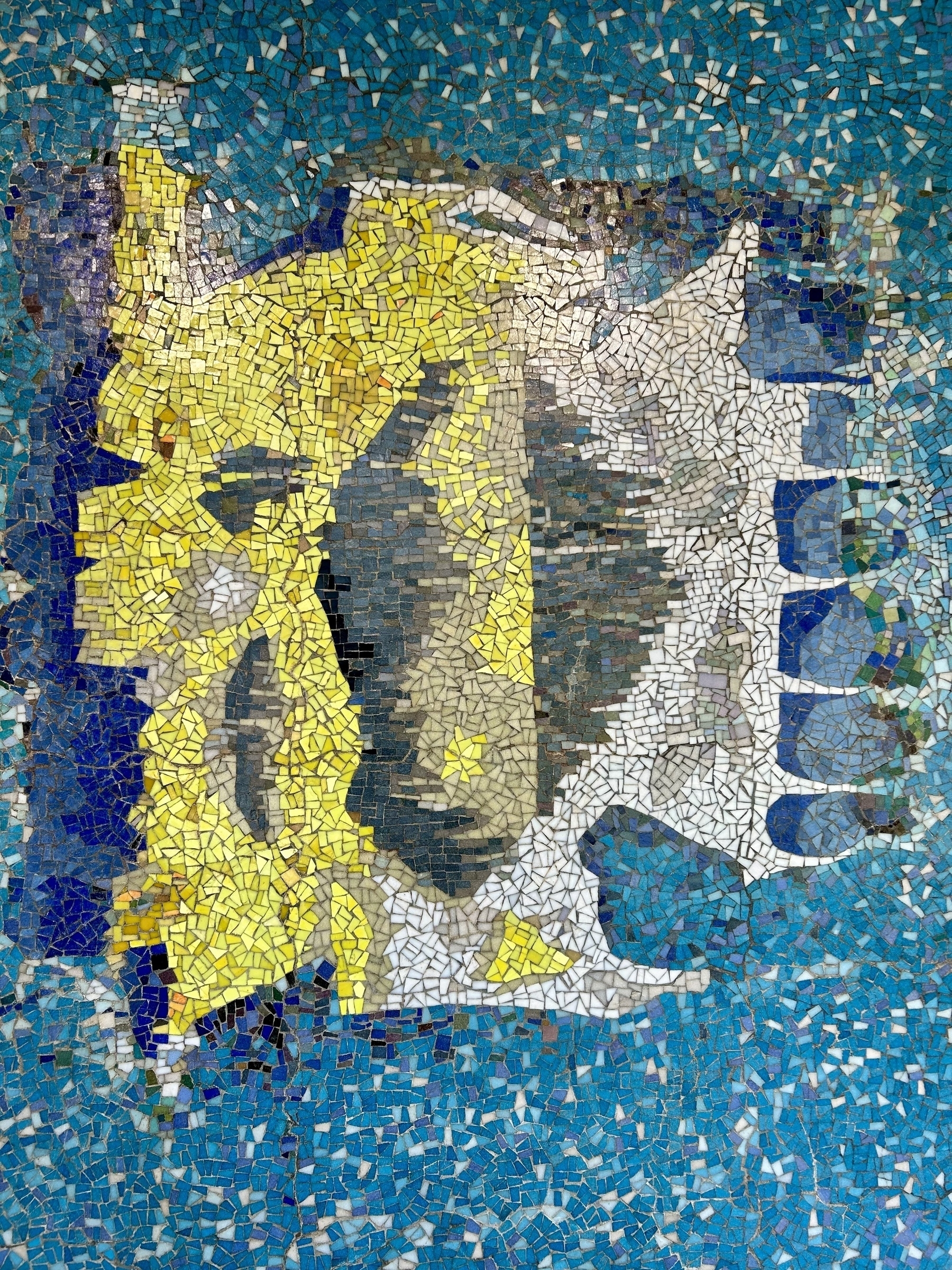 An abstract mosaic created mostly from small blue, yellow and white glass tiles. It's not meant to clearly resemble anything in particular.  