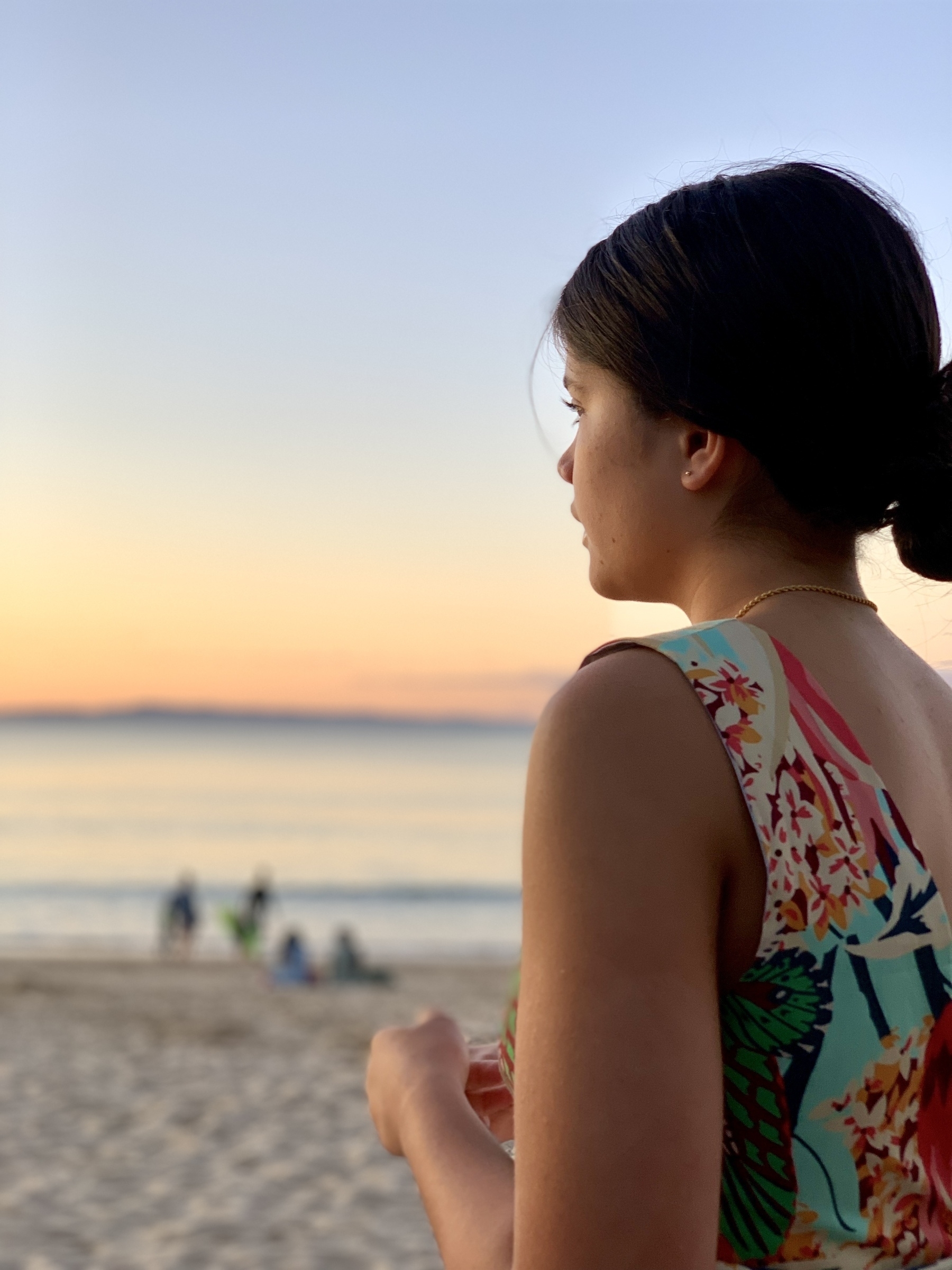 Profile of a young woman looking out over the sunset at a beach, reflected light on her face. 