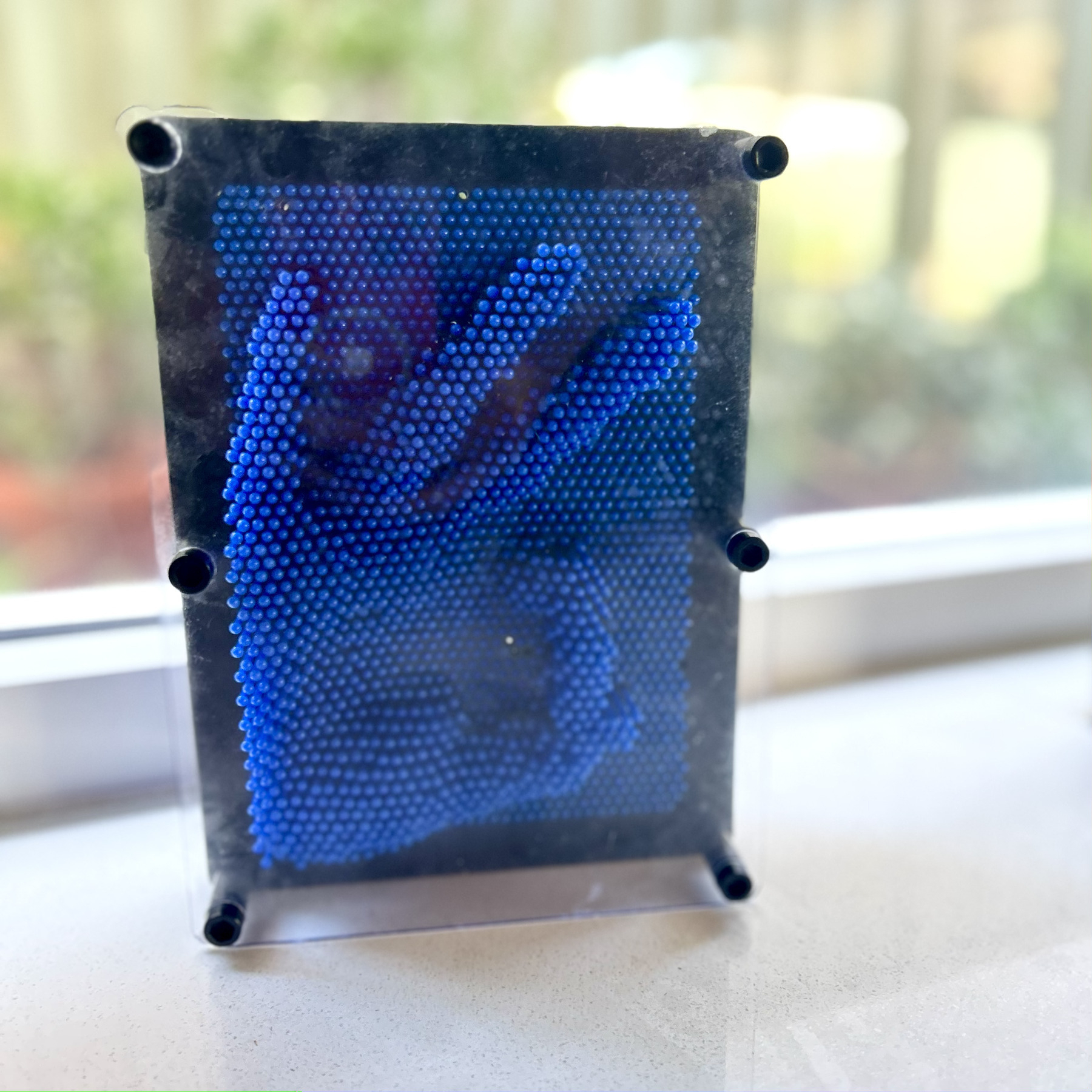 A bed of plastic blue pin-like boards, allowing you to imprint shapes. This one shows a hand giving the okay gesture with index and thumb forming a cicle, and the other three fingers splayed.