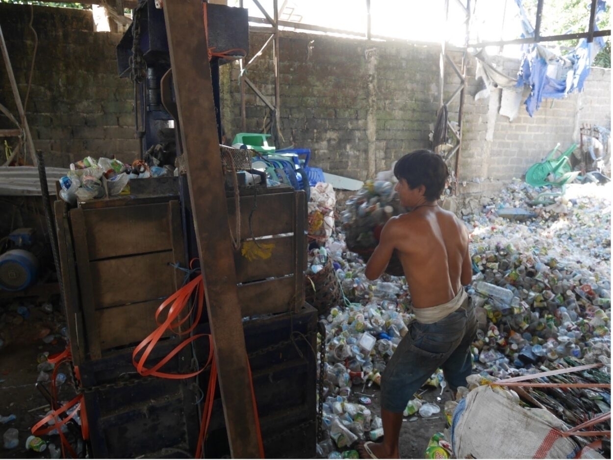 A male labourer working for a pengepul in Sumbawa feeds plastic into a press machine