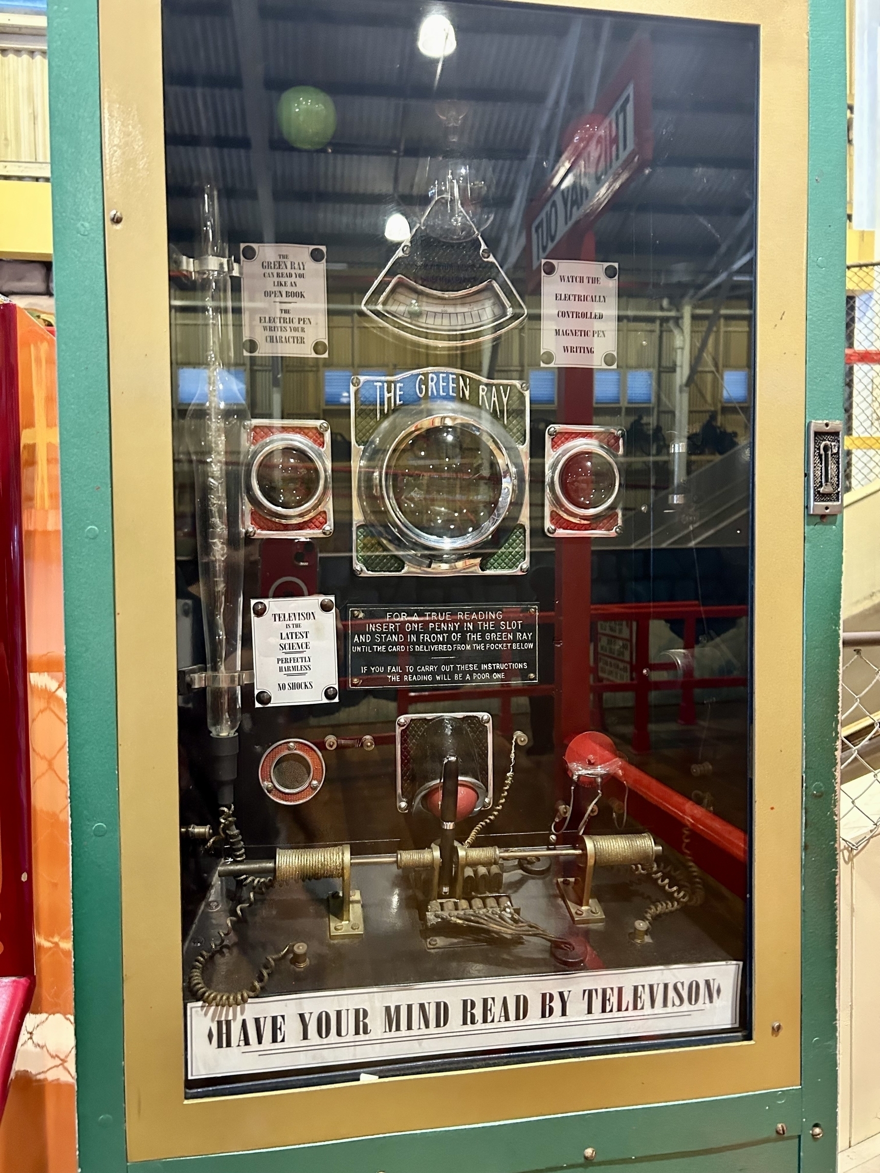 An old carnival-style fortune telling game. Multiple mechanical devices are visible inside a glass case. A label at the bottom reads "have your mind read by television". 