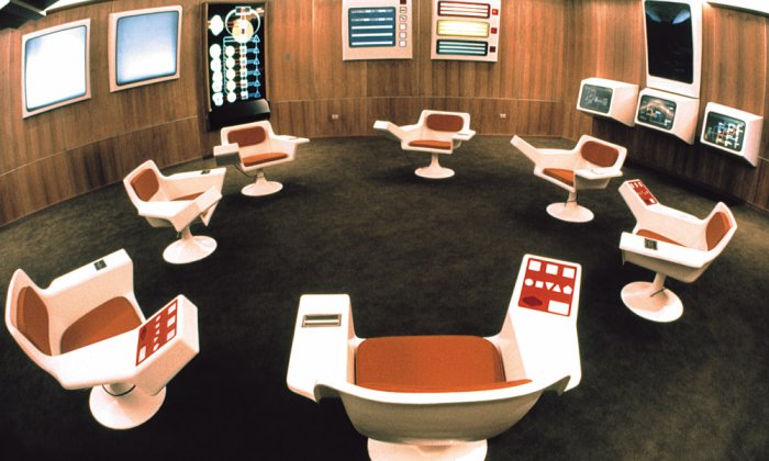 A computer-generated image of Project Cybersyn operations room. Chairs are arrnged around a room, which is decorated in iconinc 1970s style.