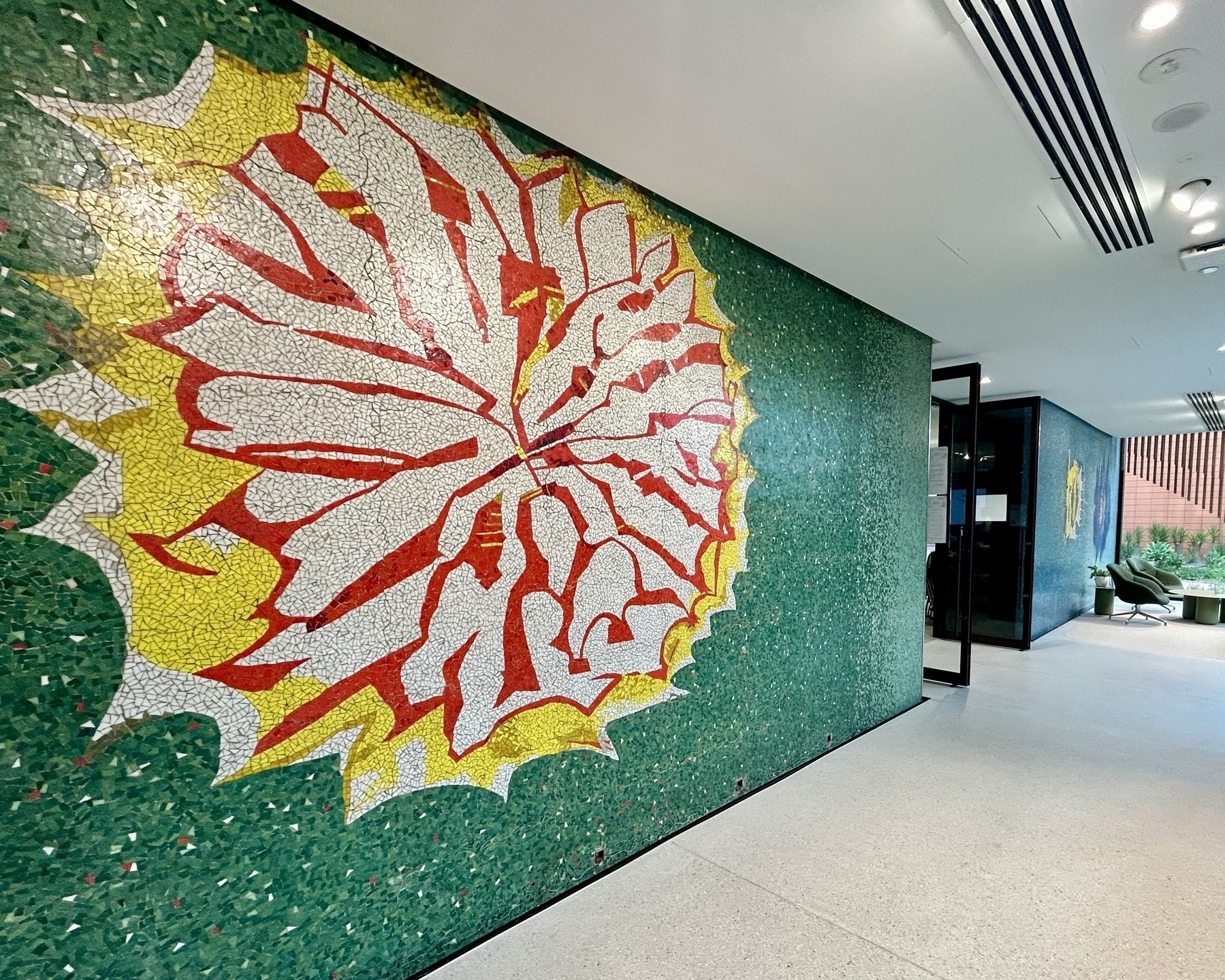 A colourful glass tile mosaic, with a yellow and red explosion-shaped feature on a speckled green wall. 
