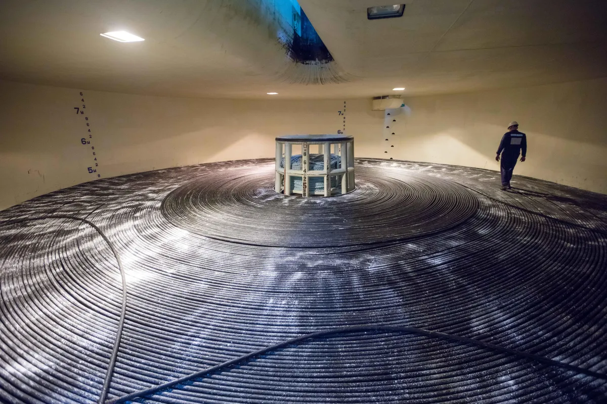 A circular room with huge amounts of spooled cable couiled up. Cable-laying ships hold hundreds of miles of cable spooled up inside three "tanks." Note the scale showing this tank to be 7 meters (22 feet) deep. This shows a segment of the Merea cable built by Microsoft and Facebook parent Meta.