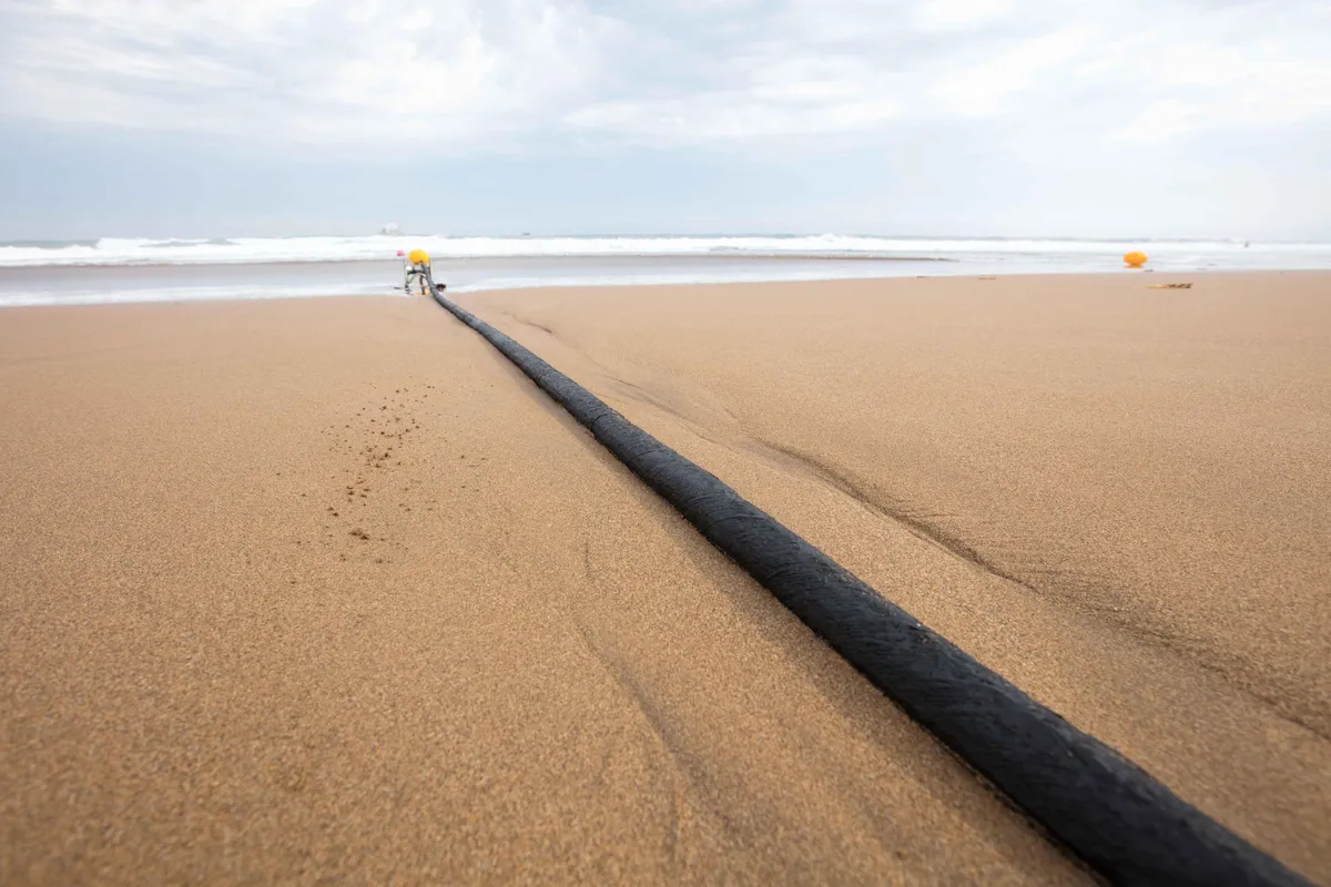 A cable running down a beach into the ocean. The Marea cable from Microsoft and Meta is high-tech enough to carry 200 terabits of data per second, but employs centuries-old nautical technology too: It's coated in tar.