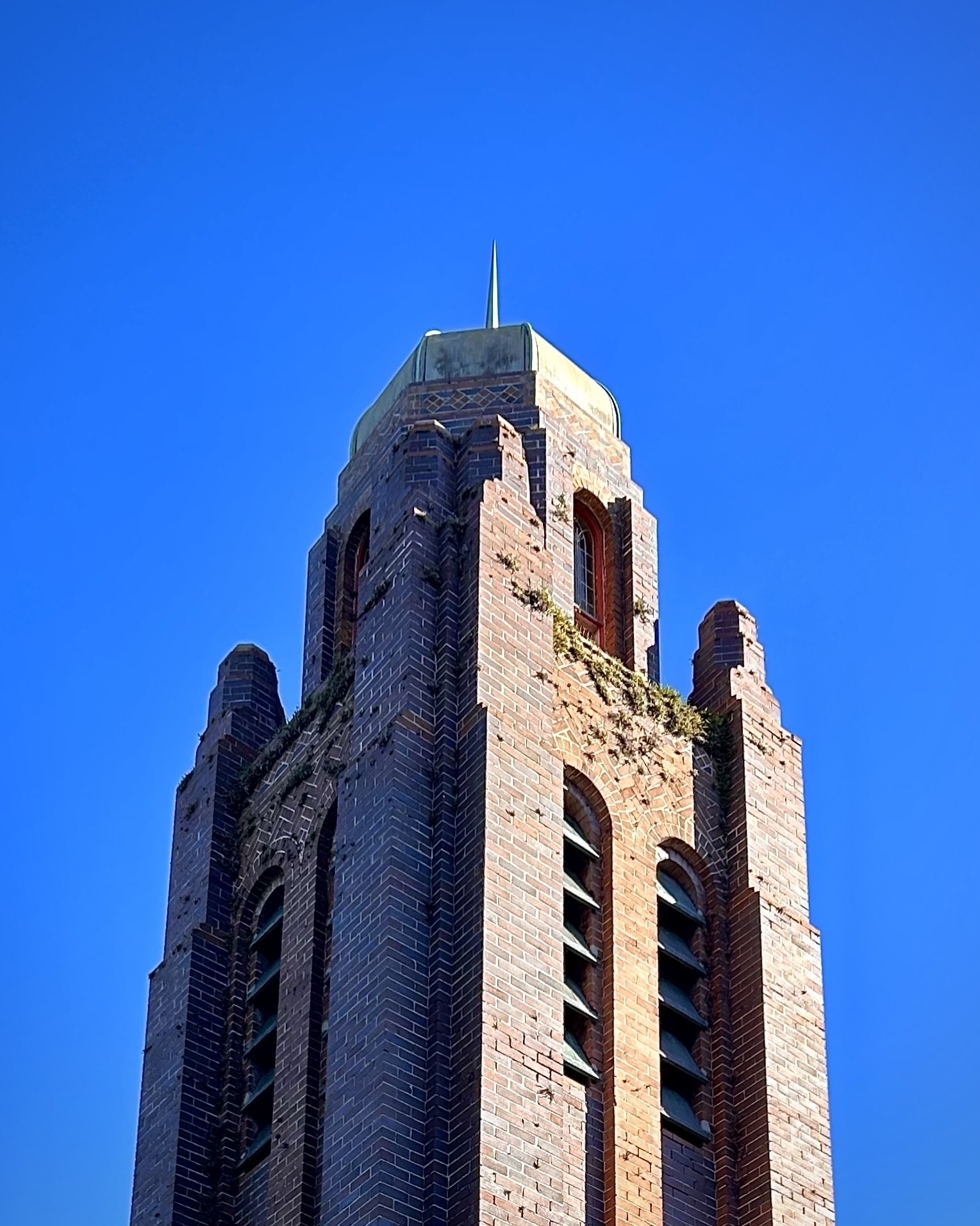A deco-like brick spire on top of a church, with blue sky in the background.  