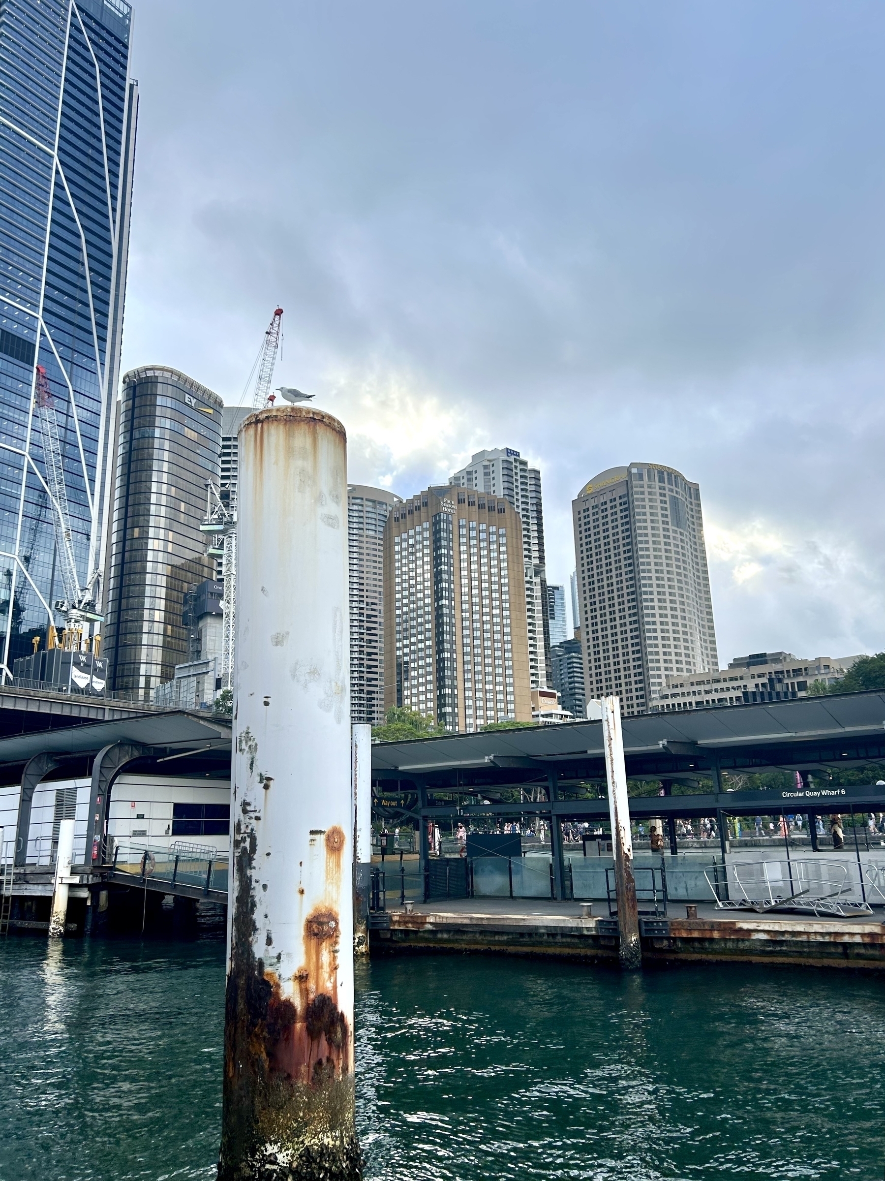 Sydney skyline at Circular Quay, with a rusty pylon in the foreground looking similar in scale to the buildings. 