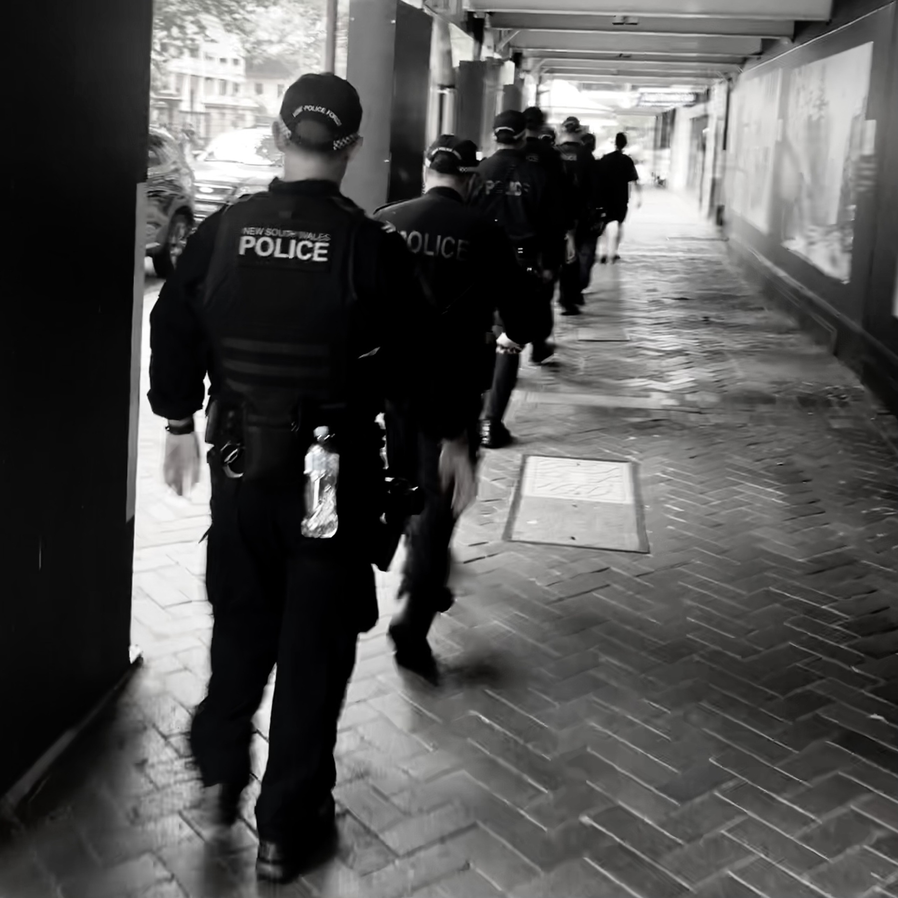 A black and white image of New South Wales public order police walking in single file down a footpath. 