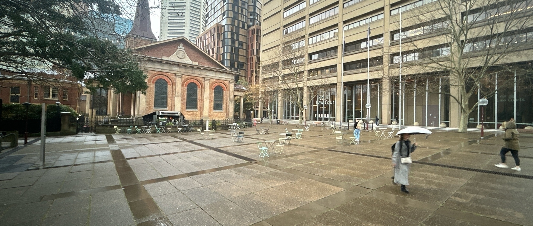 A paved square with some figures walking across it. A church is visible in the background. 