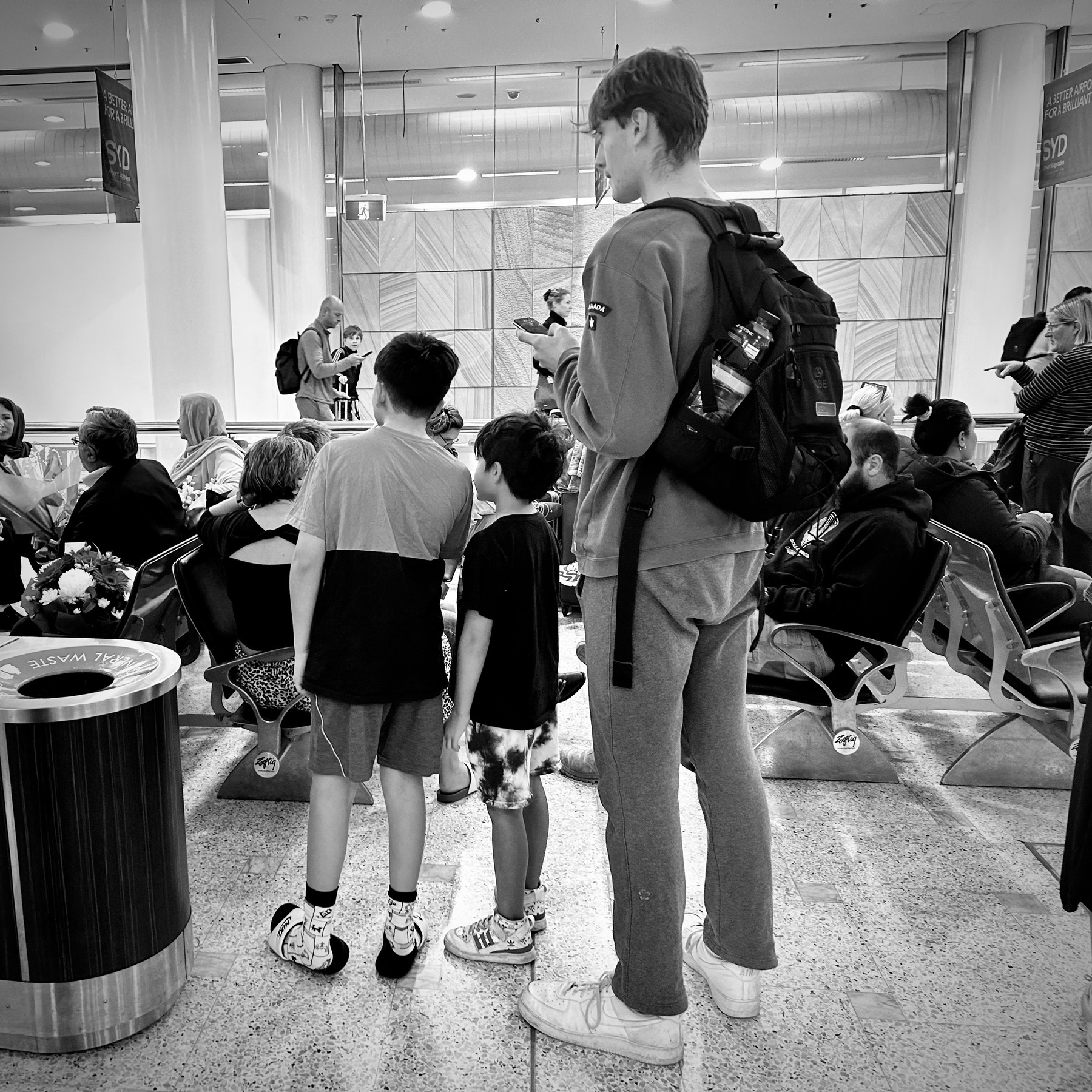 Three boys waiting at the airport. Two are shorter, one is very tall. 