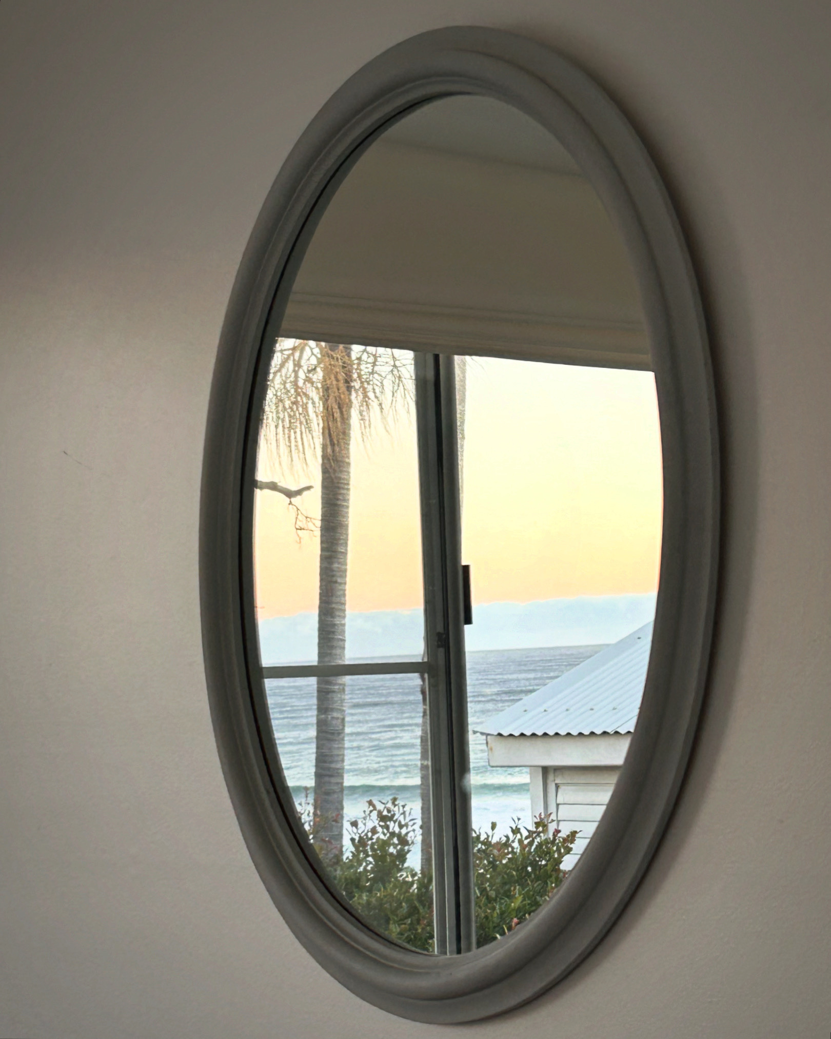 A circular mirror, reflecting a view of the ocean in the distance 