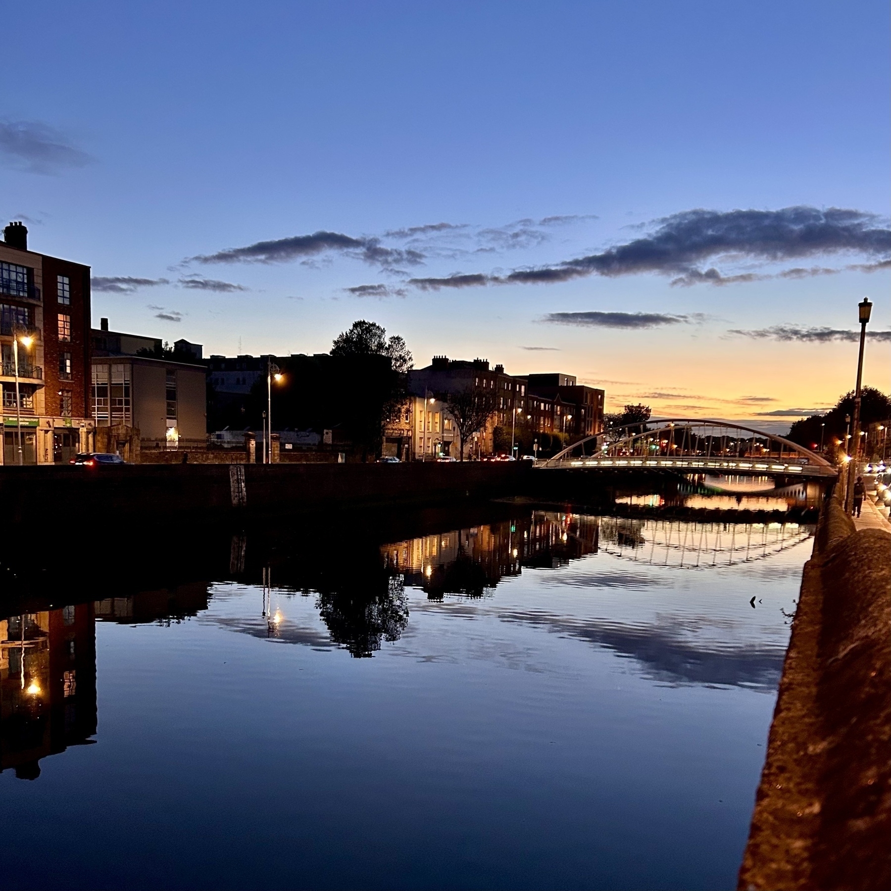 An angle arched bridge over a river at sunset. The blue and yellow sky is reflected in the River Liffey. 