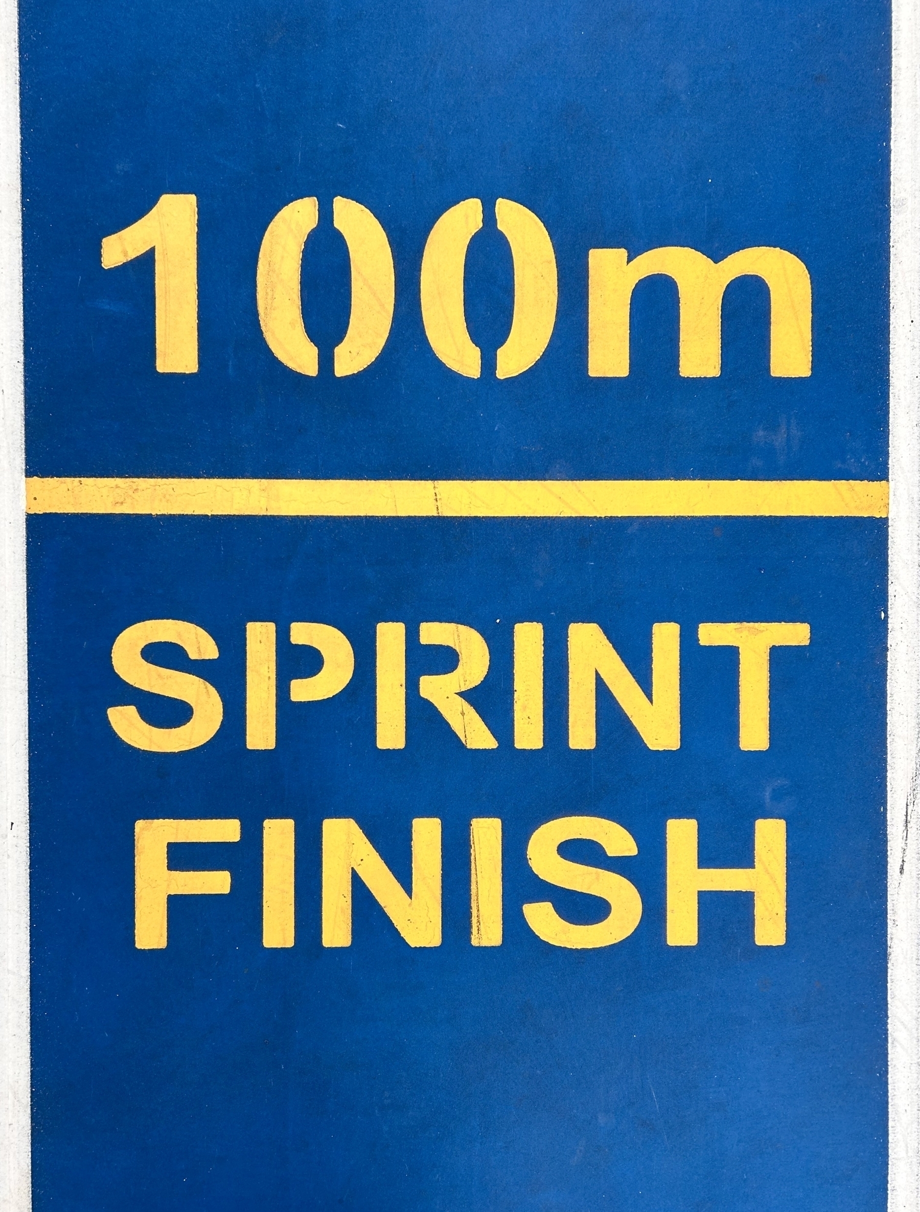 A line on concrete. Stencilled above and below it is "100m SPRINT FINISH"