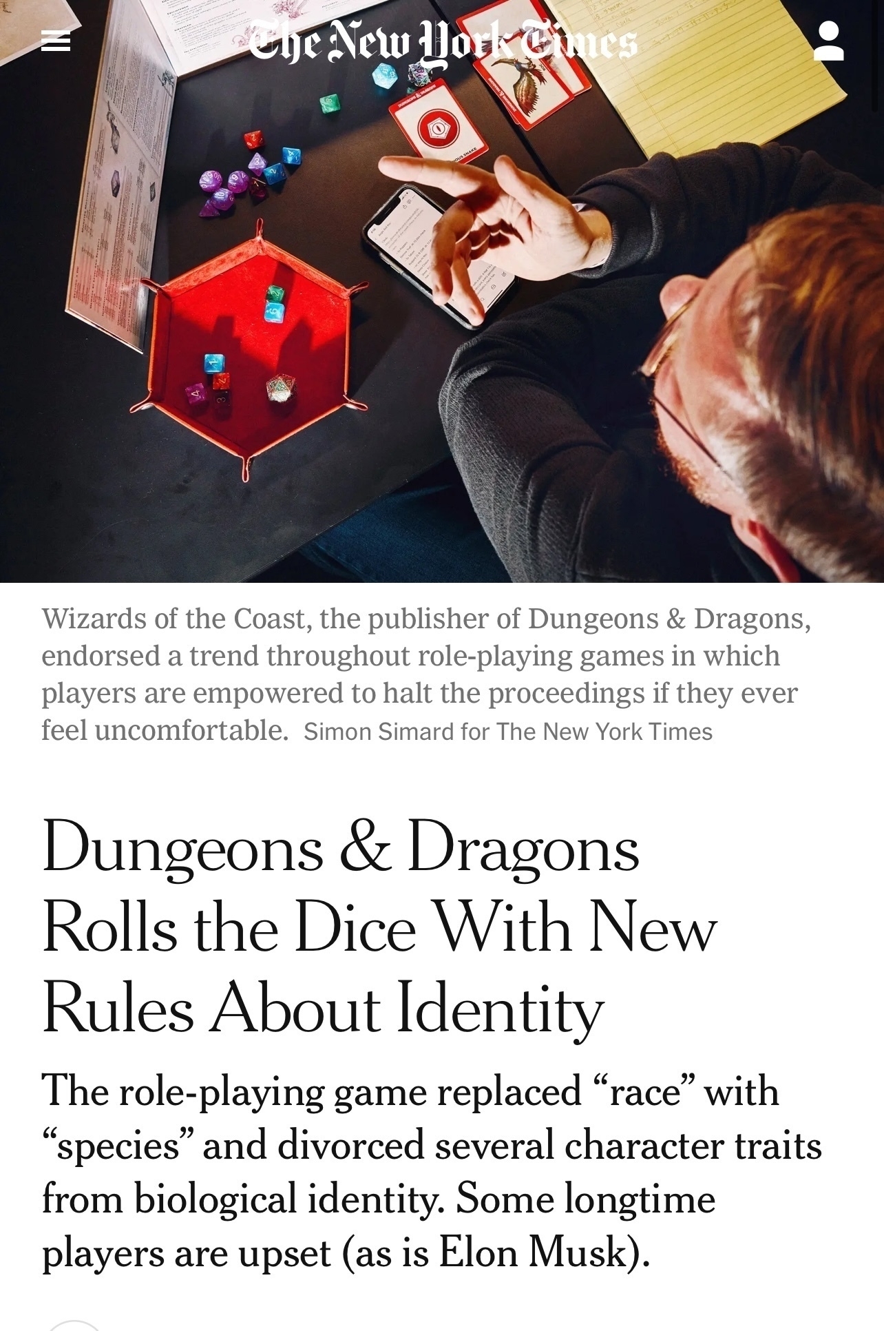 Screenshot of a New York Times article. The image is a top-down view of dice and a dungeon master screen, typical of a Dungeons and Dragons game. The text is:&10;&10;Heading: Dungeons & Dragons&10;Rolls the Dice With New Rules About Identity&10;&10;Image caption text (oddly not very descriptive of the image itself): Wizards of the Coast, the publisher of Dungeons & Dragons, endorsed a trend throughout role-playing games in which players are empowered to halt the proceedings if they ever feel uncomfortable. Simon Simard for The New York Times&10;&10;Body text: The role-playing game replaced "race" with&10;"species" and divorced several character traits from biological identity. Some longtime players are upset (as is Elon Musk).