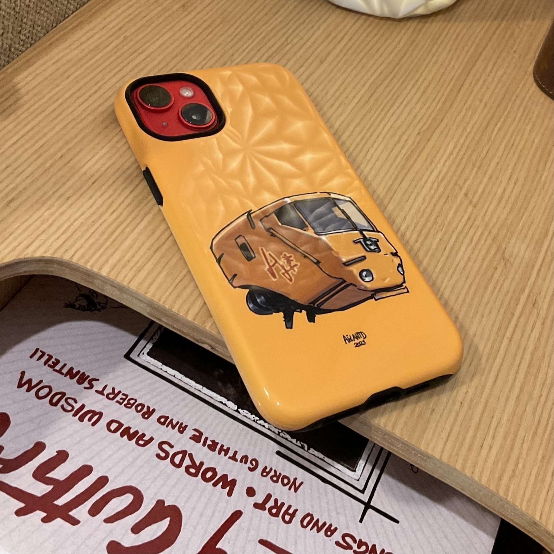 A yellow phone case with a bright yellow flying square minivan-like vehicle, which is typical of Ailantd's style of illustration. 
