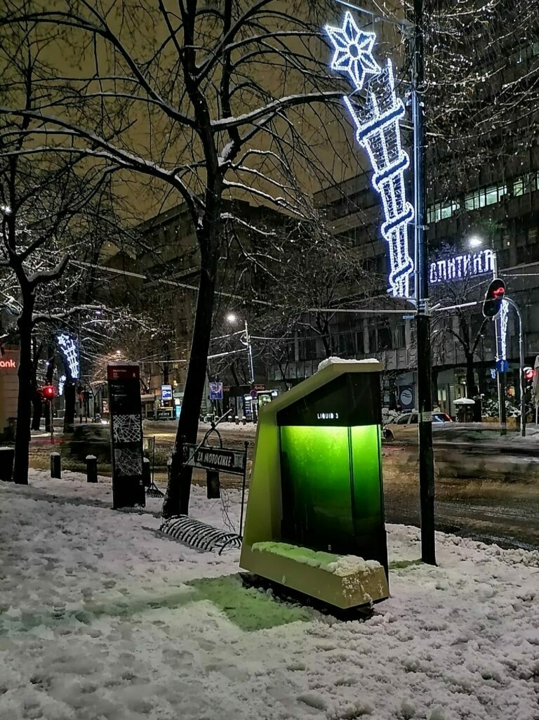 A narrow glass box filled with a bright green liquid, on a snowy street at night.