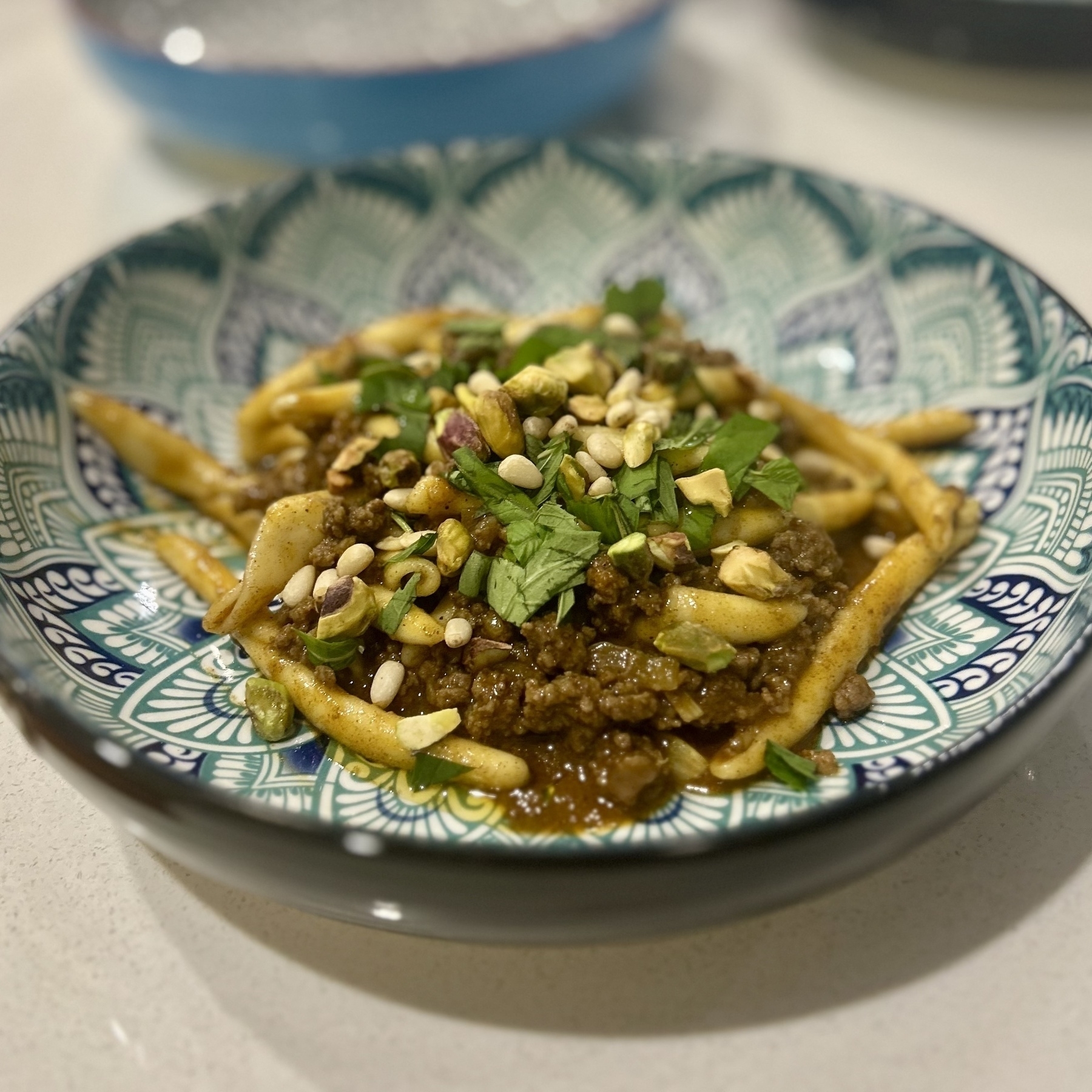 A bowl of pasta with a fairly thick sauce, mint and pine nuts and pistachios on top. 