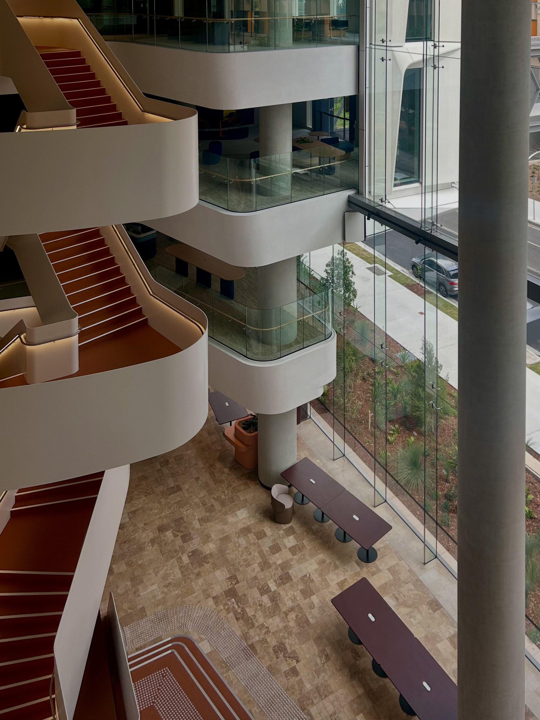 A building interior void with curved balconies, red-carpeted stairs, and a glass wall. 