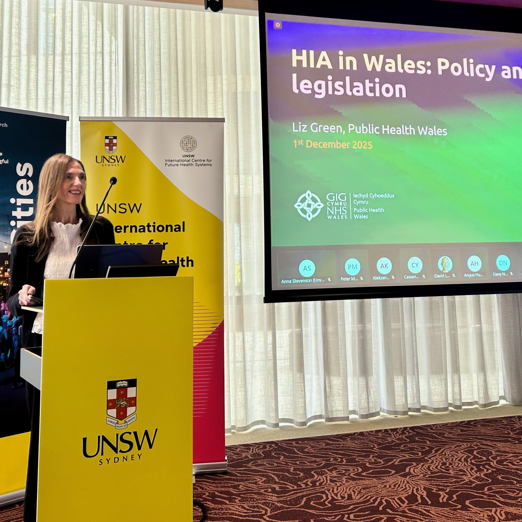 Dr Liz Green is standing at a podium giving a presentation on HIA in Wales: Policy and Legislation at UNSW Sydney.