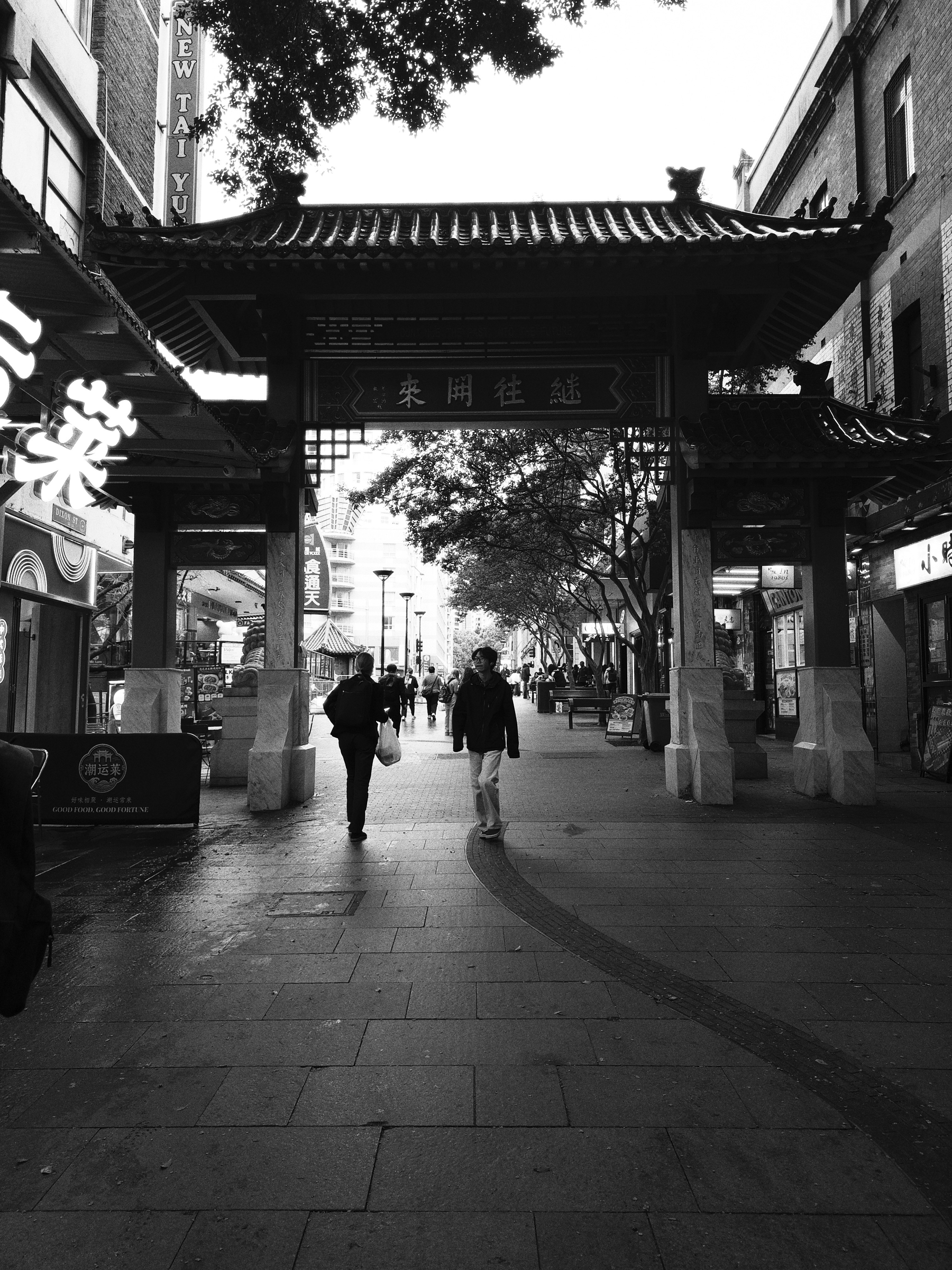 A traditional Chinese-style gate stands at the entrance of a pedestrian street lined with shops and people walking underneath it. It’s Chinatown in Sydney. 