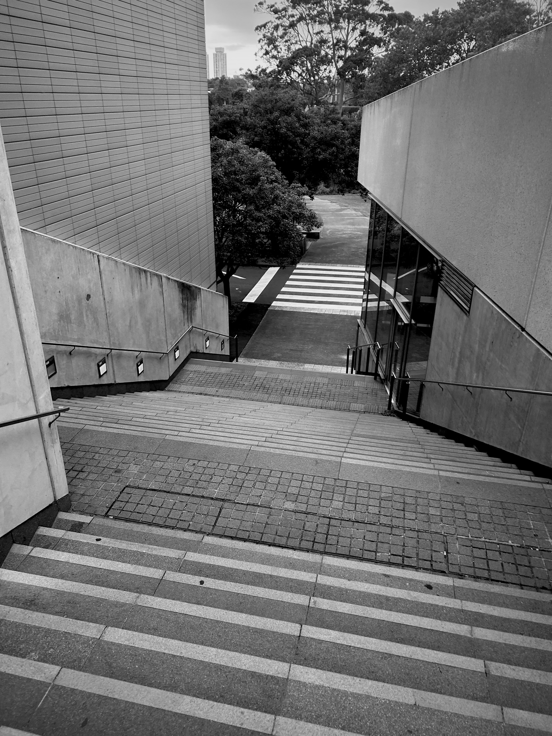 A set of wide stairs leads down between modern buildings towards a crosswalk surrounded by trees.