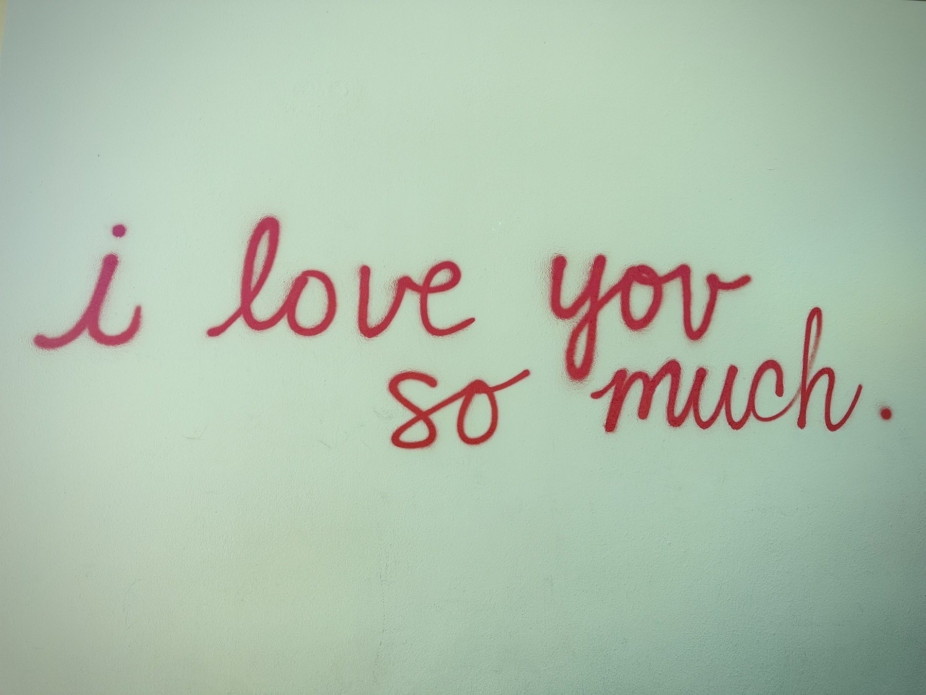 A light green stucco wall with 'i love you so much.' written in red cursive spray paint. Outside Jo's Coffee in Austin, Texas.