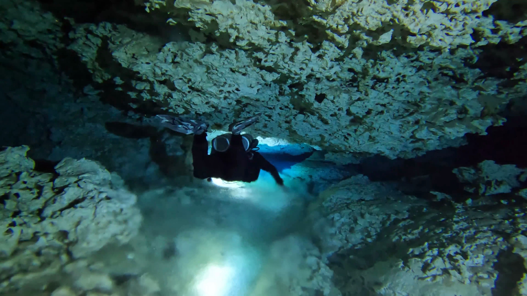 A diver swimming through a brightly lit white pock marked cave, their hand dragging through the halocline mixing the fresh and salt water layers, trailing a blurry interface behind them.