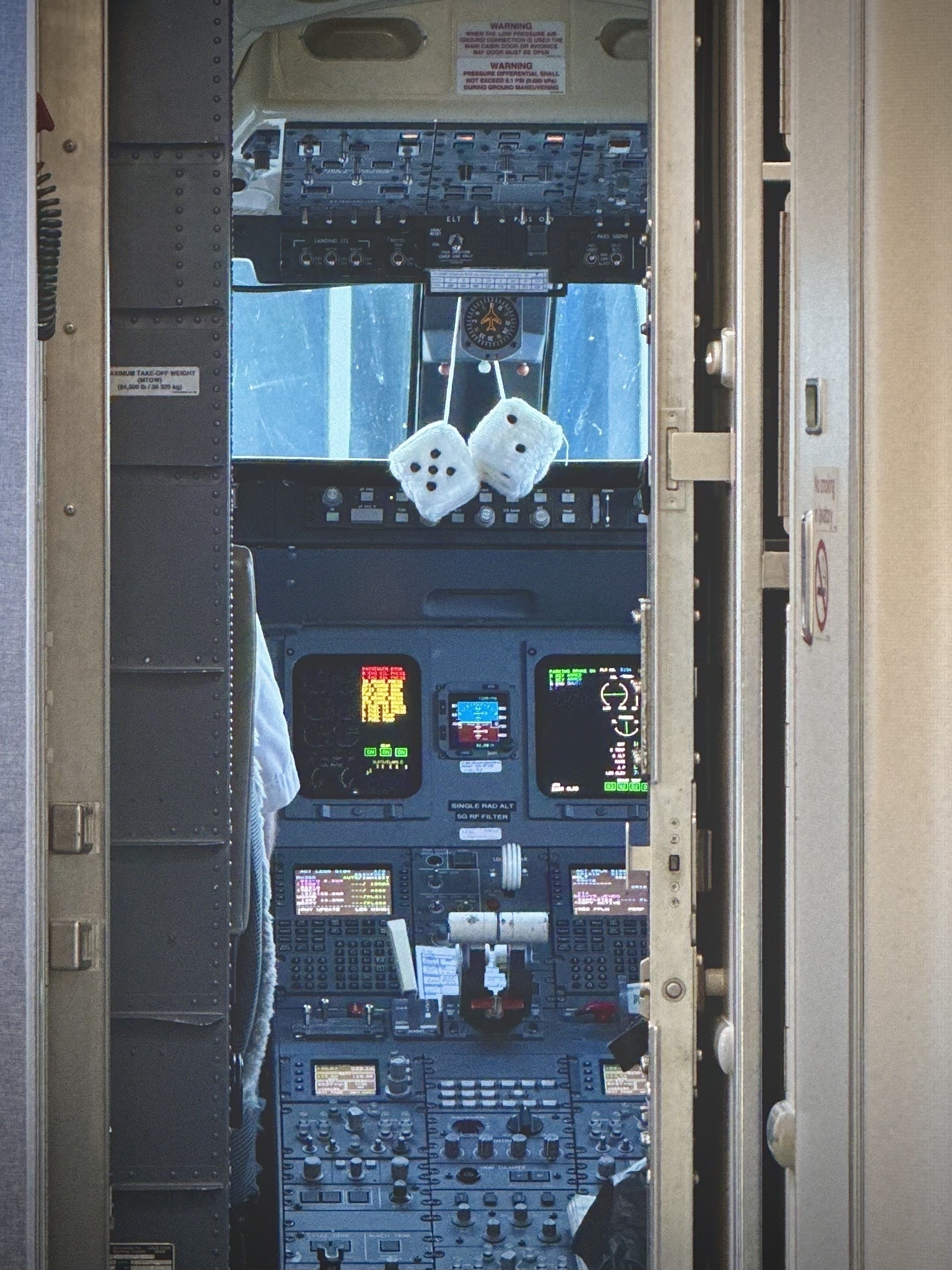 Through the door of a cockpit, some fuzzy dice hang above the flight controls.